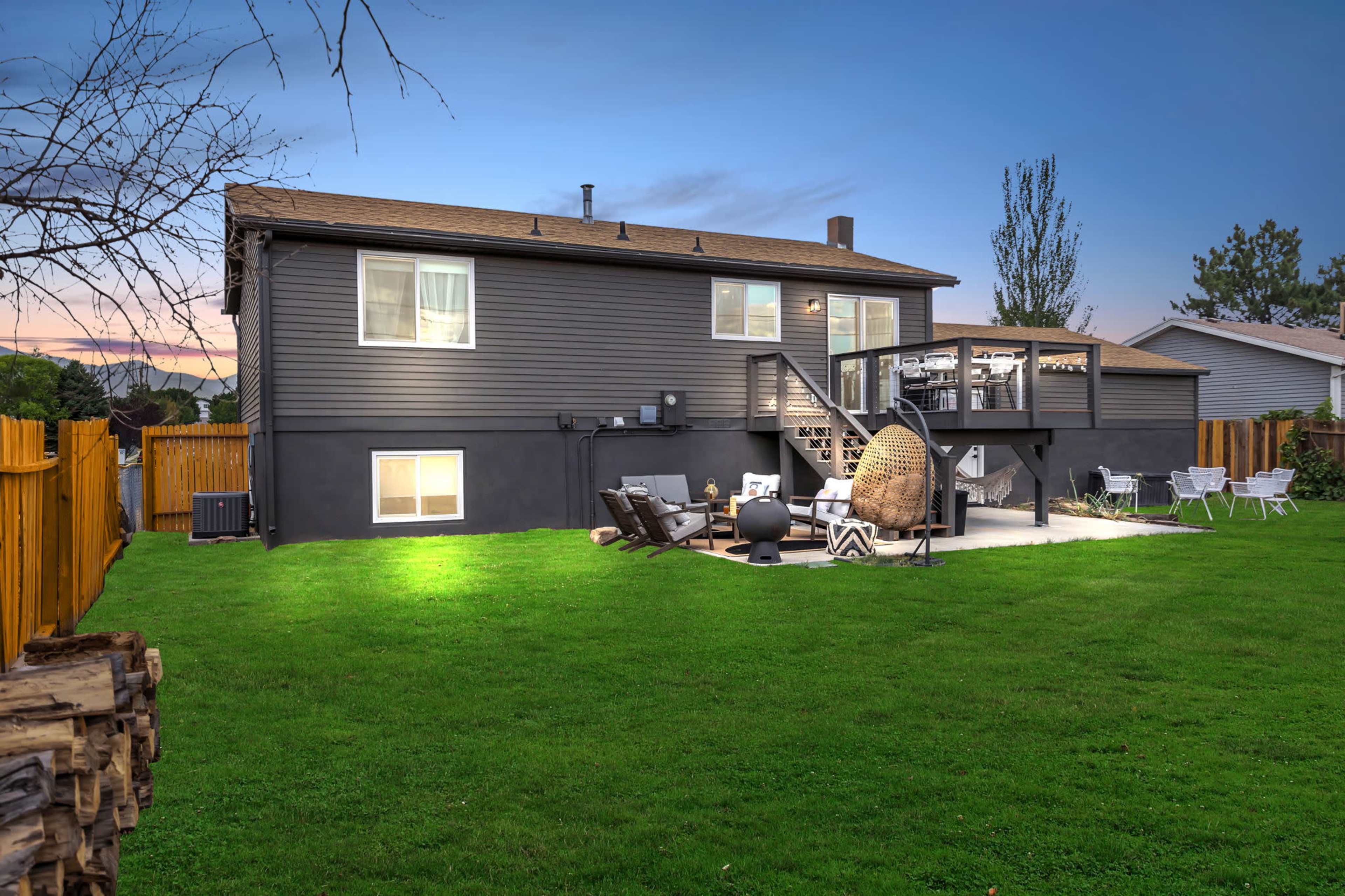 A two-story gray house with a wooden deck and a spacious backyard featuring outdoor furniture and a fire pit.