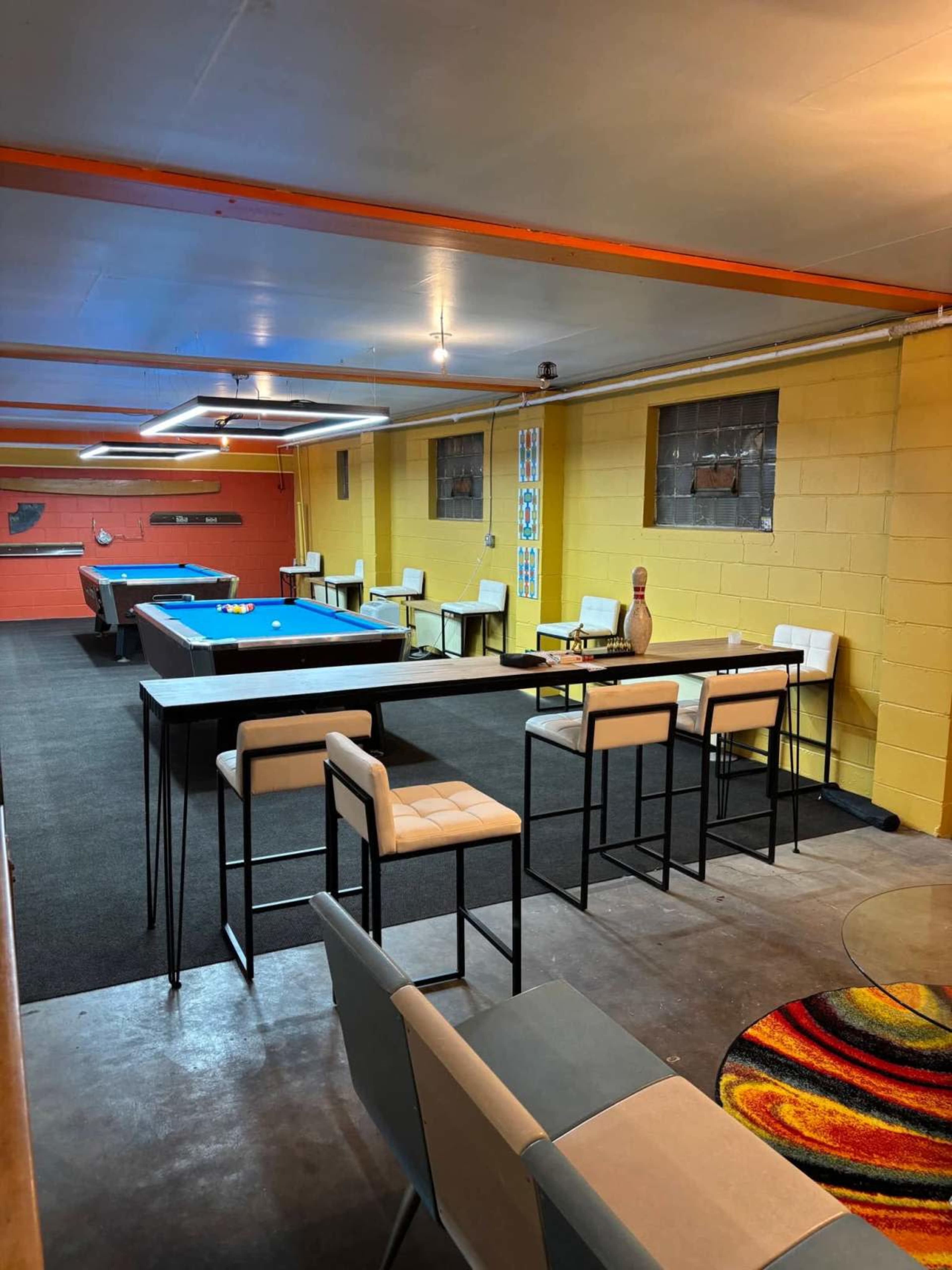 The image shows a recreational room with a pool table, seating areas, and bold yellow walls.