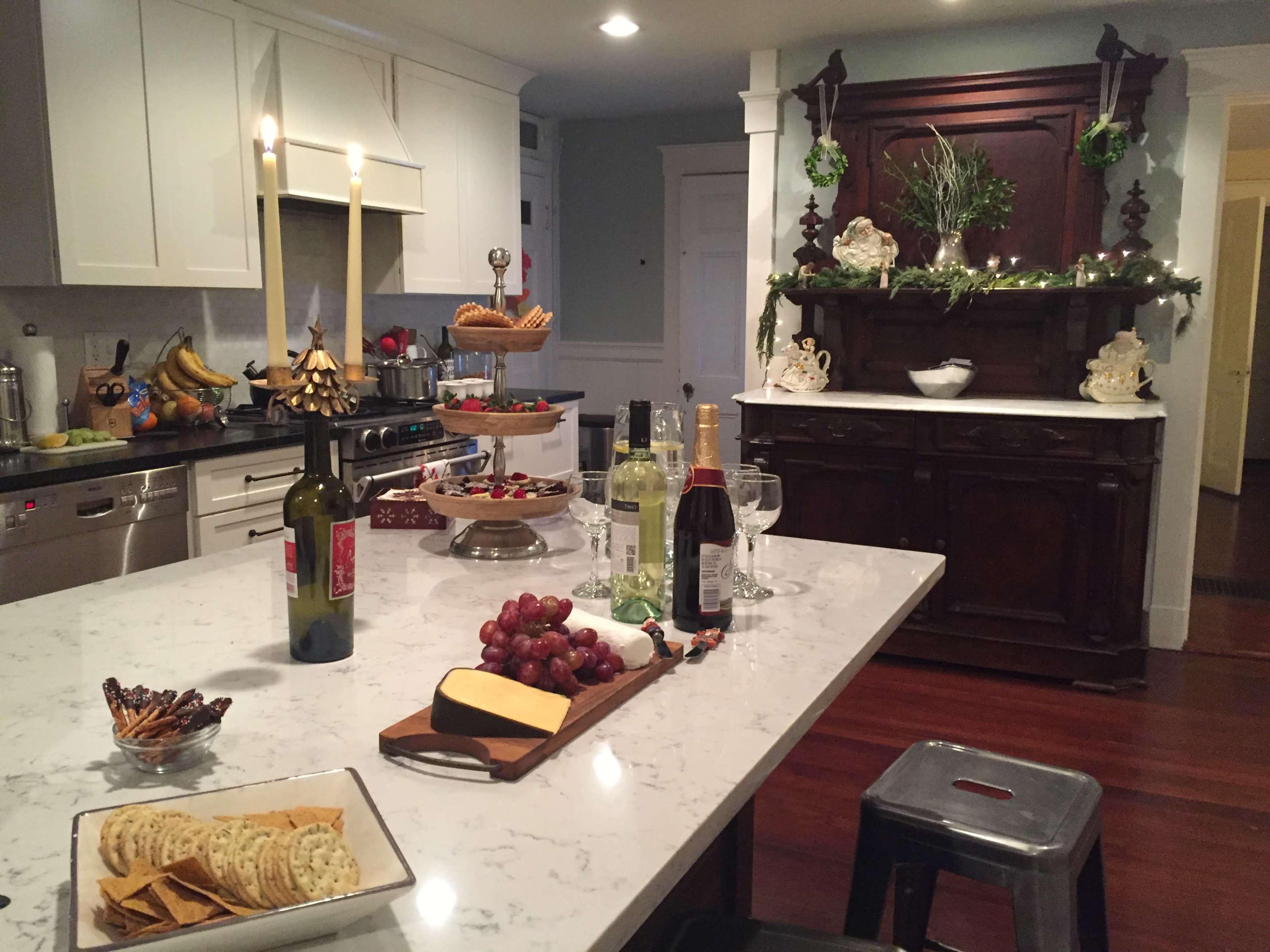 A kitchen featuring a marble countertop with wine, grapes, crackers, and a variety of appetizers, alongside an elegantly decorated dining area.