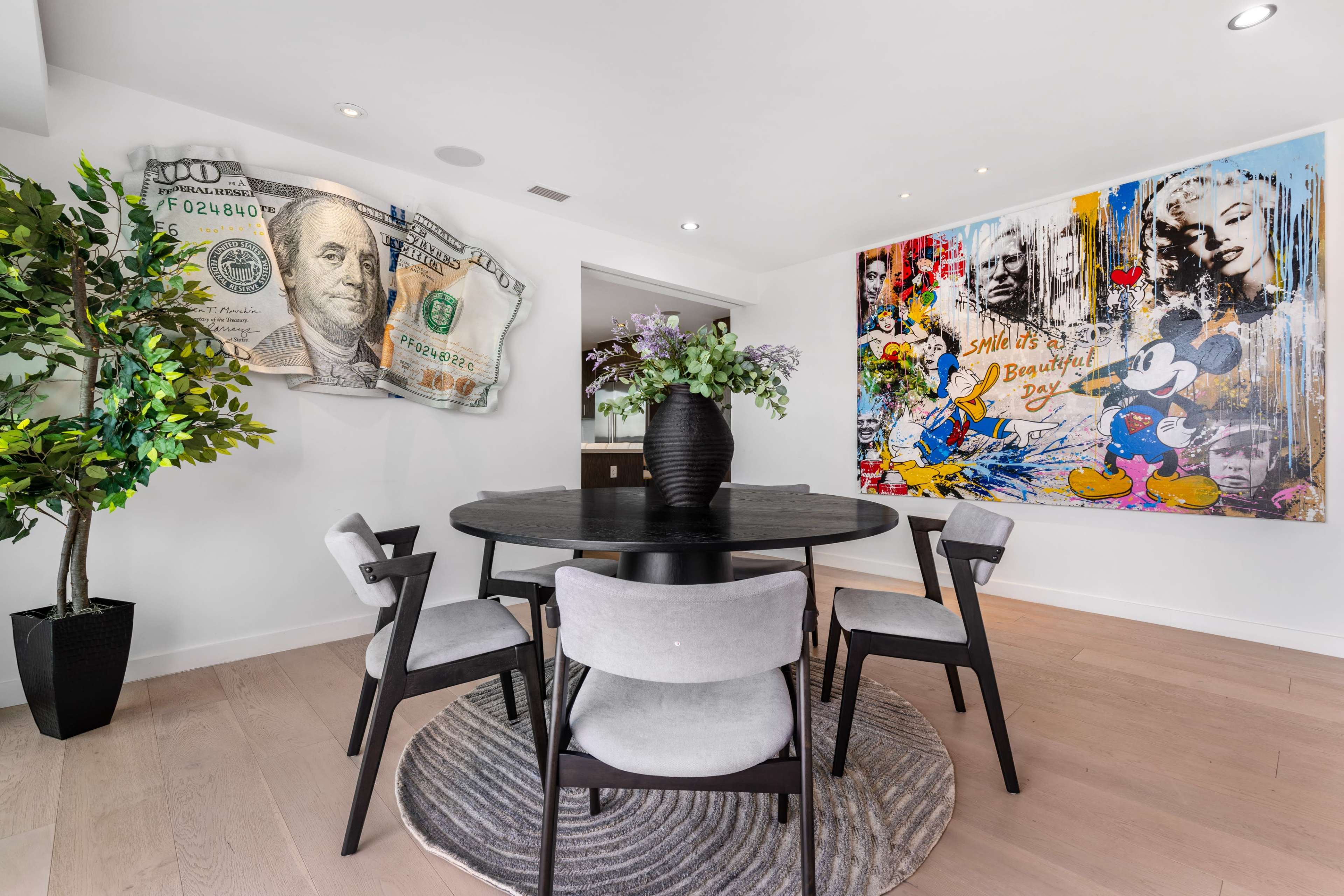 A modern dining area features a round black table surrounded by four chairs, with a large art piece and a decorative plant on display.