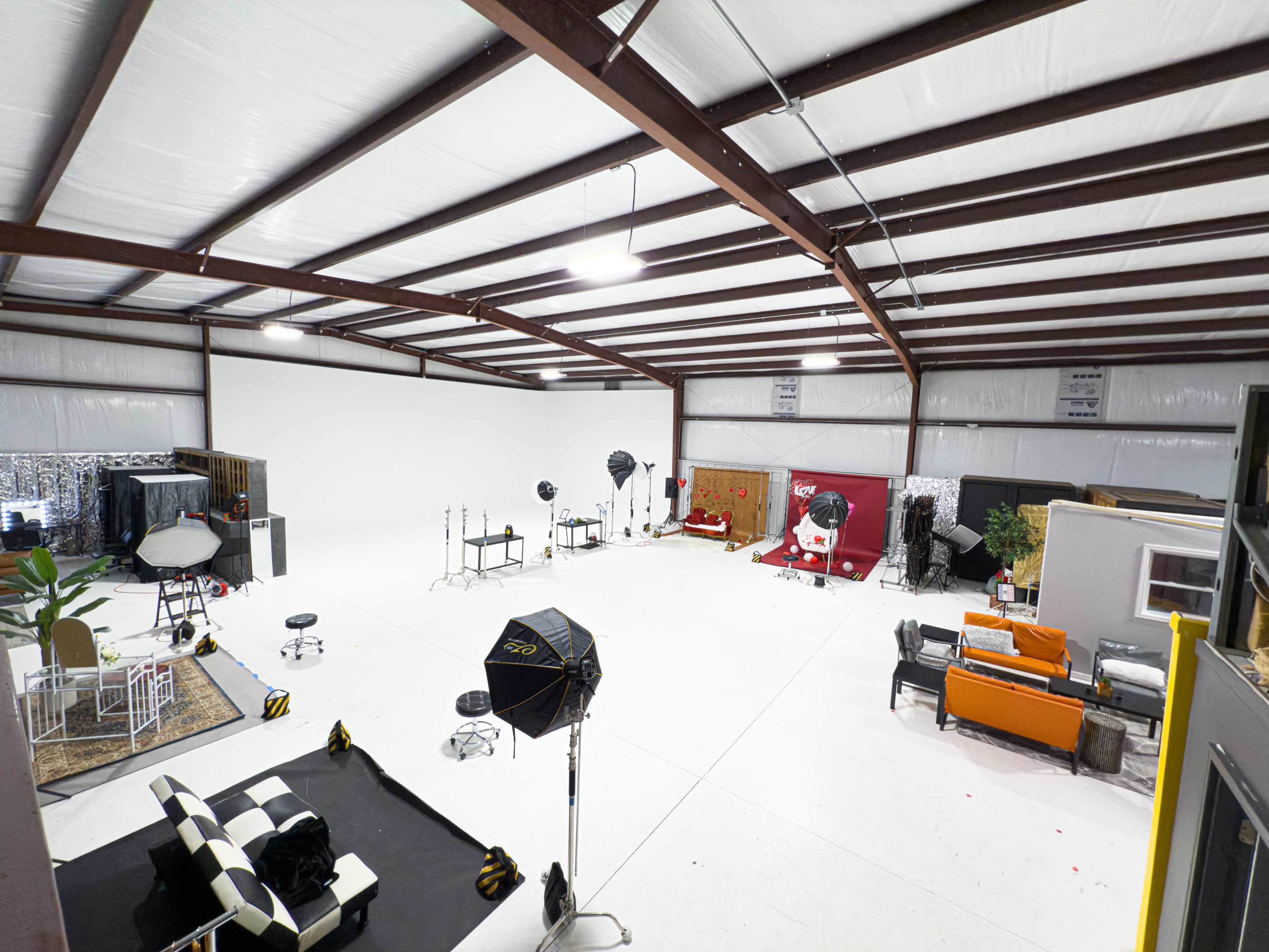 The image shows a large, empty studio space with various photography equipment and seating arrangements scattered throughout.