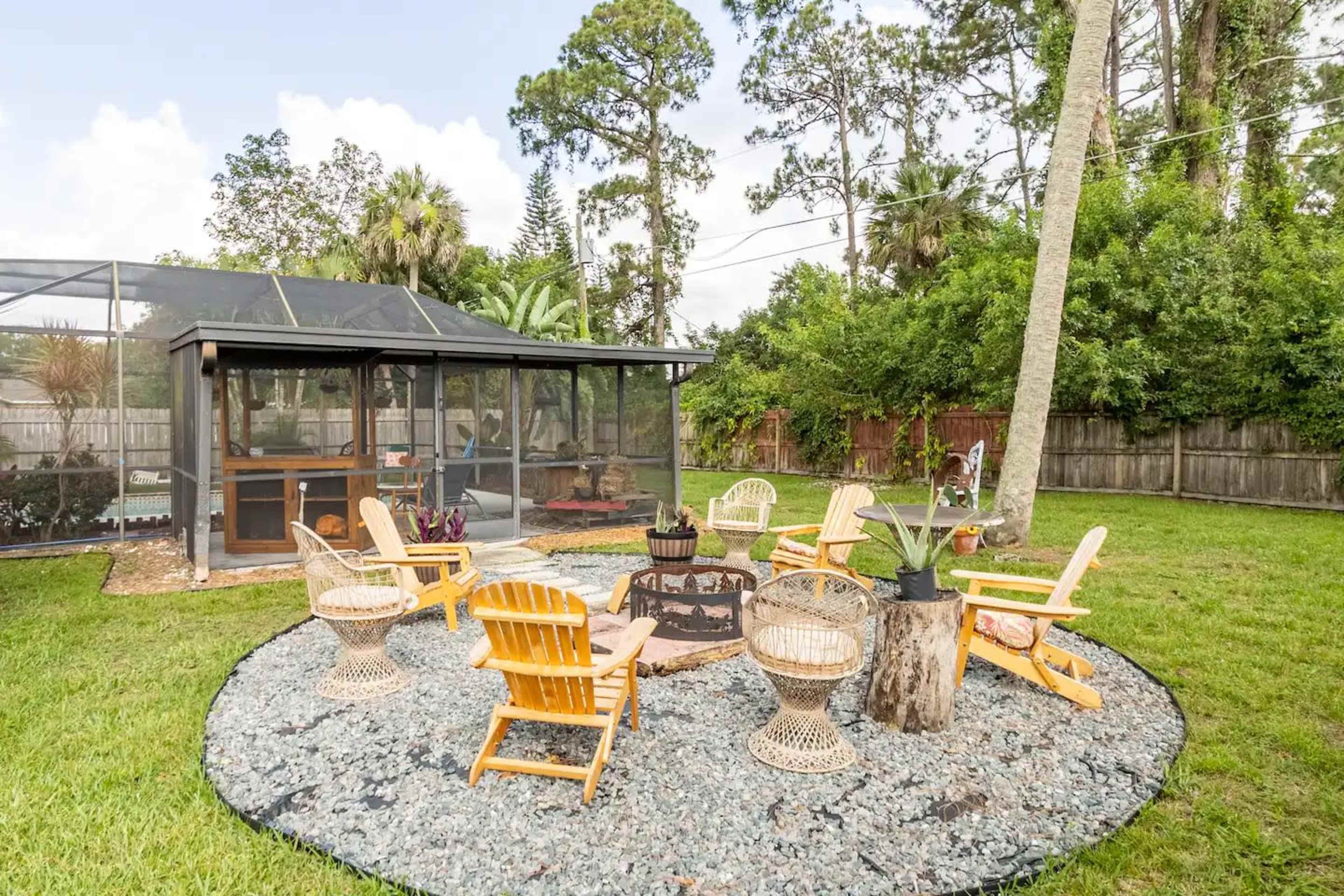 A circular seating area with wooden chairs and a fire pit is surrounded by a landscaped yard with a screened gazebo in the background.