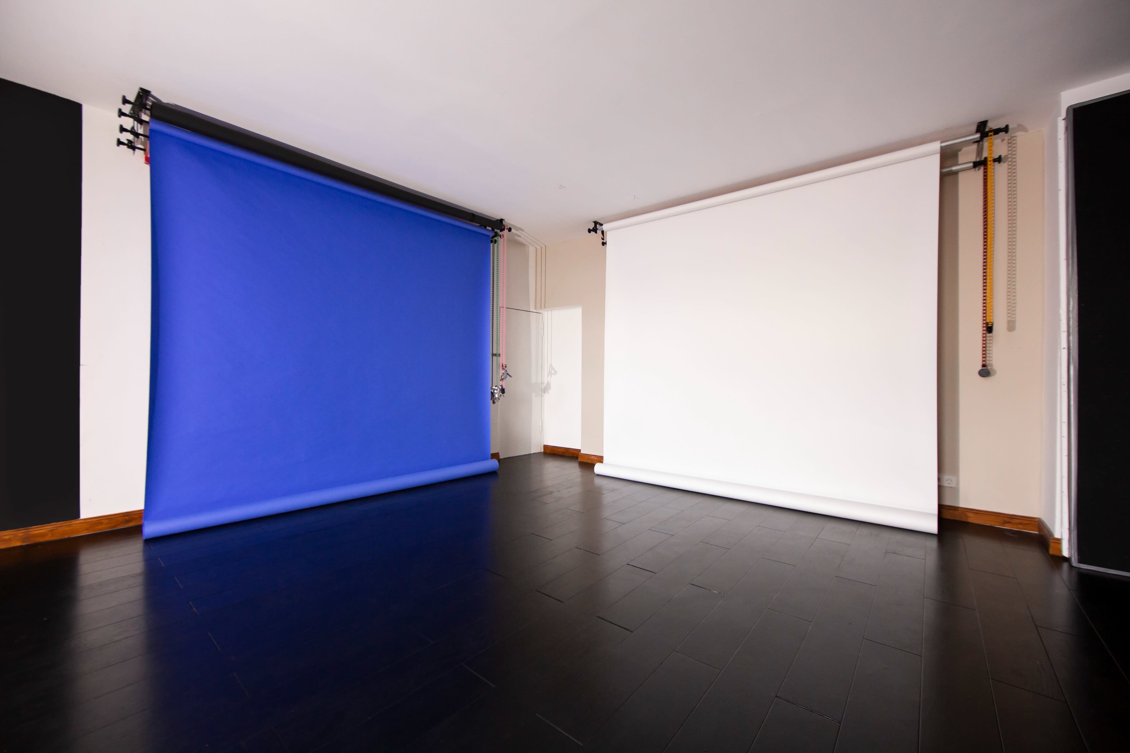 A photography studio with a blue backdrop on the left and a white backdrop on the right, placed against a dark wooden floor.