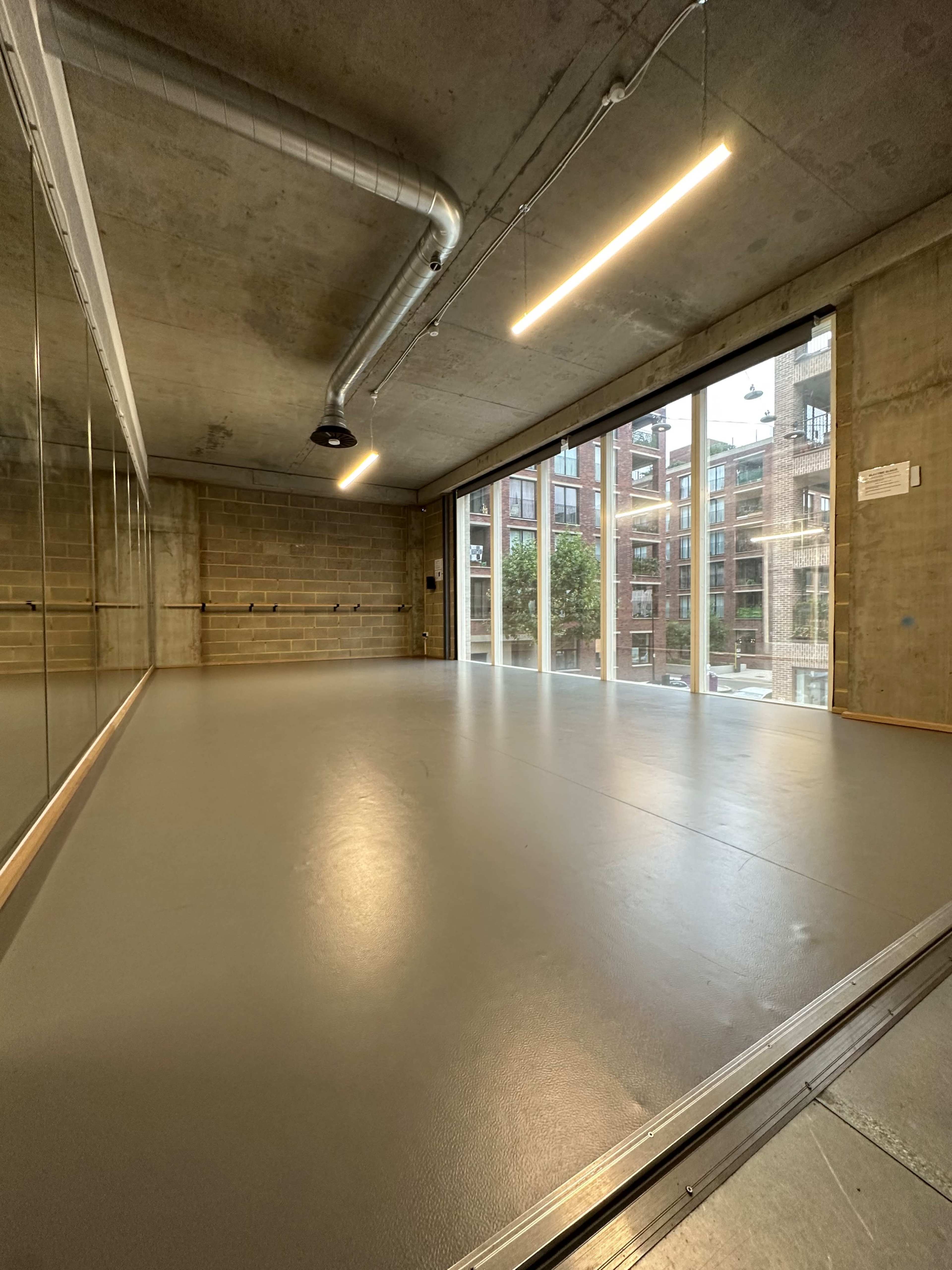 A spacious room with large windows, concrete walls, and a smooth floor, reflecting an industrial design.