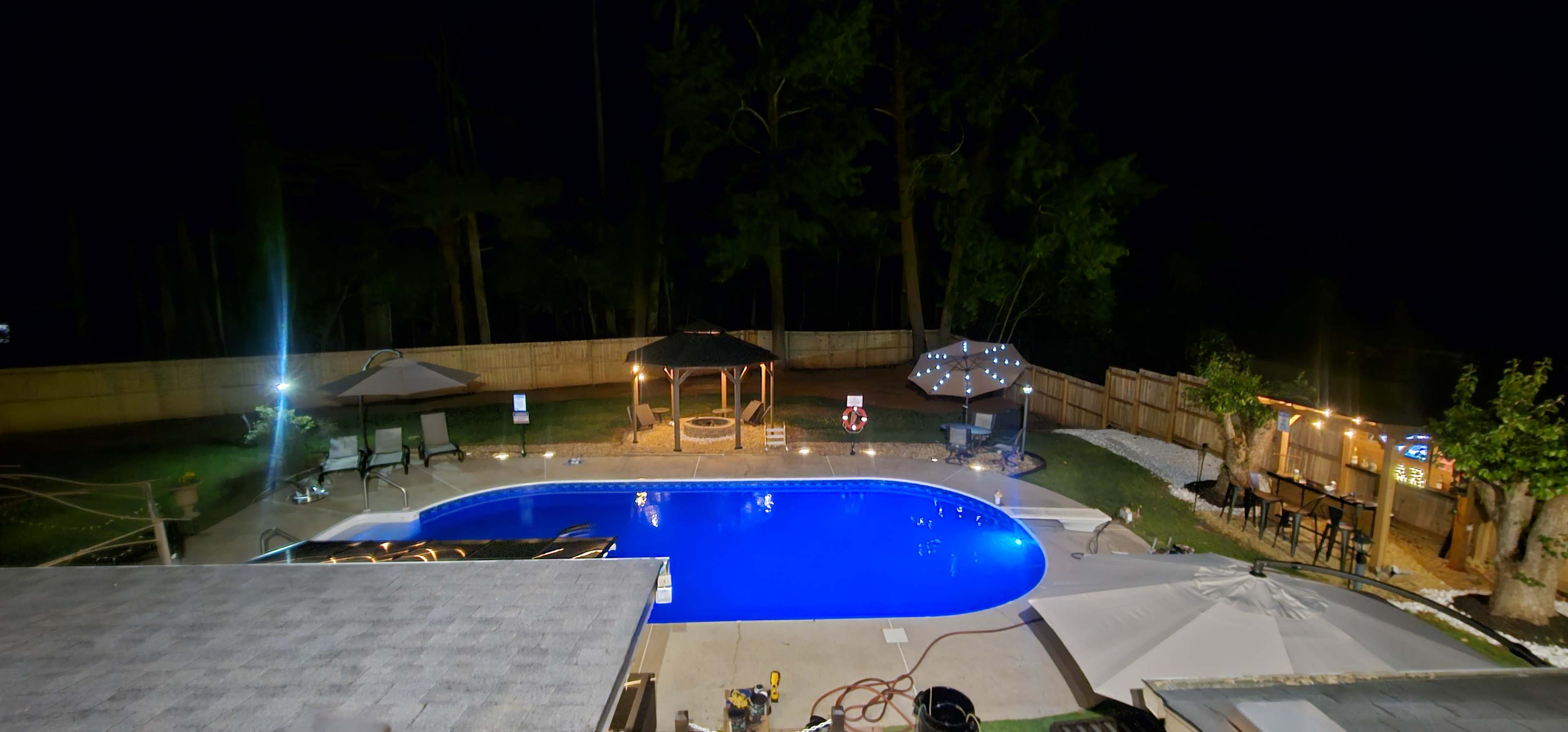 A brightly lit swimming pool surrounded by landscaped areas, seating, and decorative features at night.