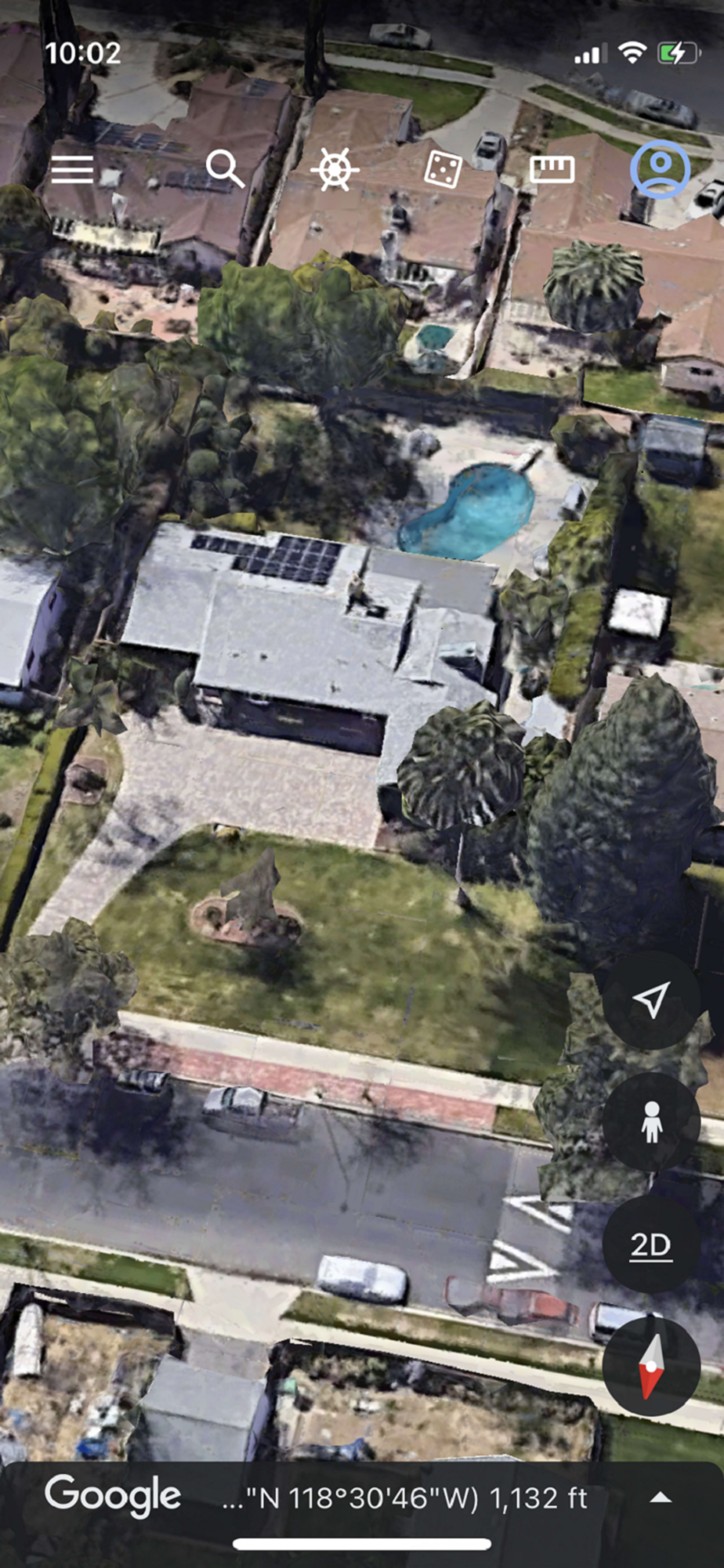 The image shows an aerial view of a suburban property featuring a house with a lawn, palm trees, a swimming pool, and surrounding residential homes.