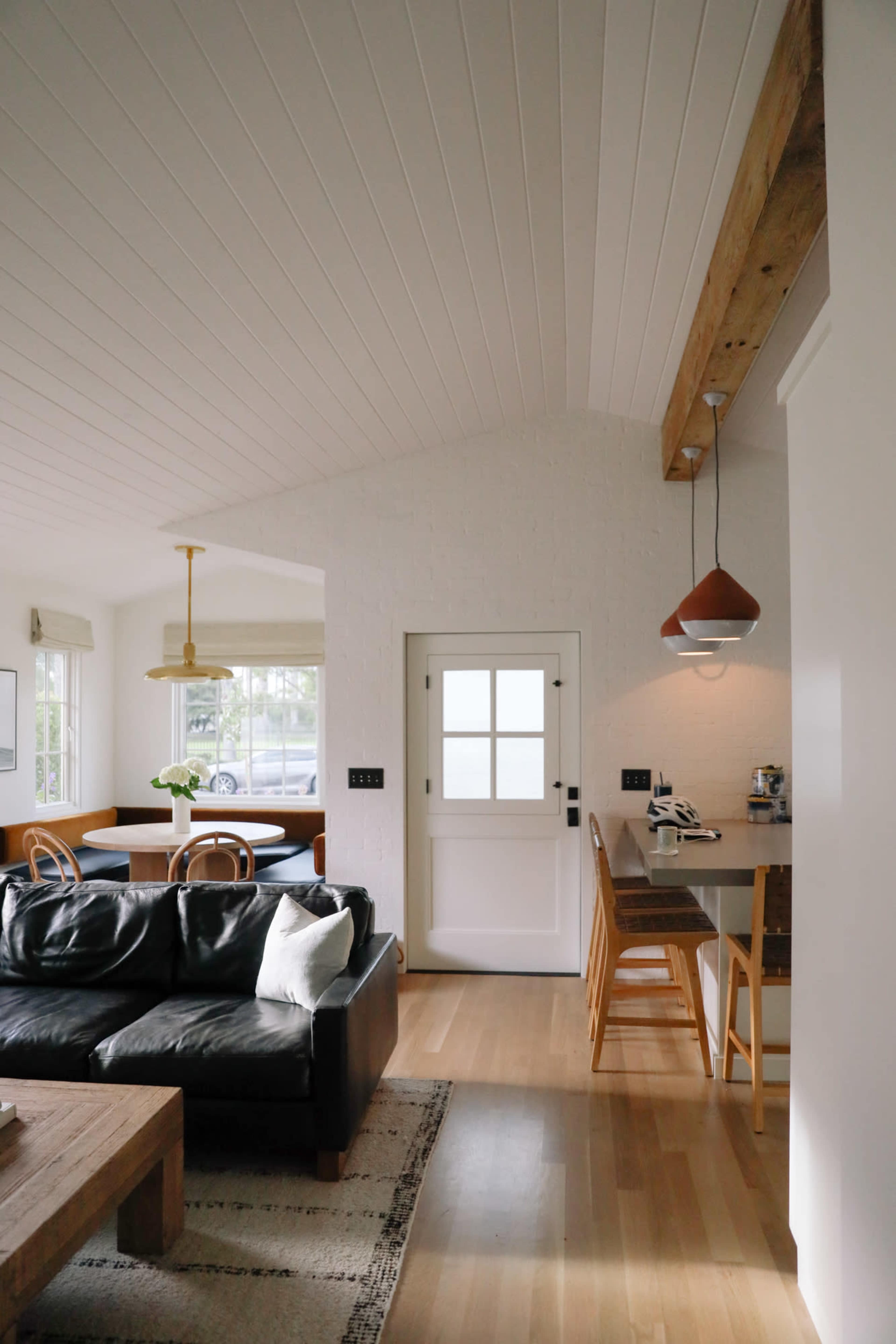 A modern living area features a black leather sofa, a wooden coffee table, and an open kitchen with a bar area adjacent to a dining space with a large window.