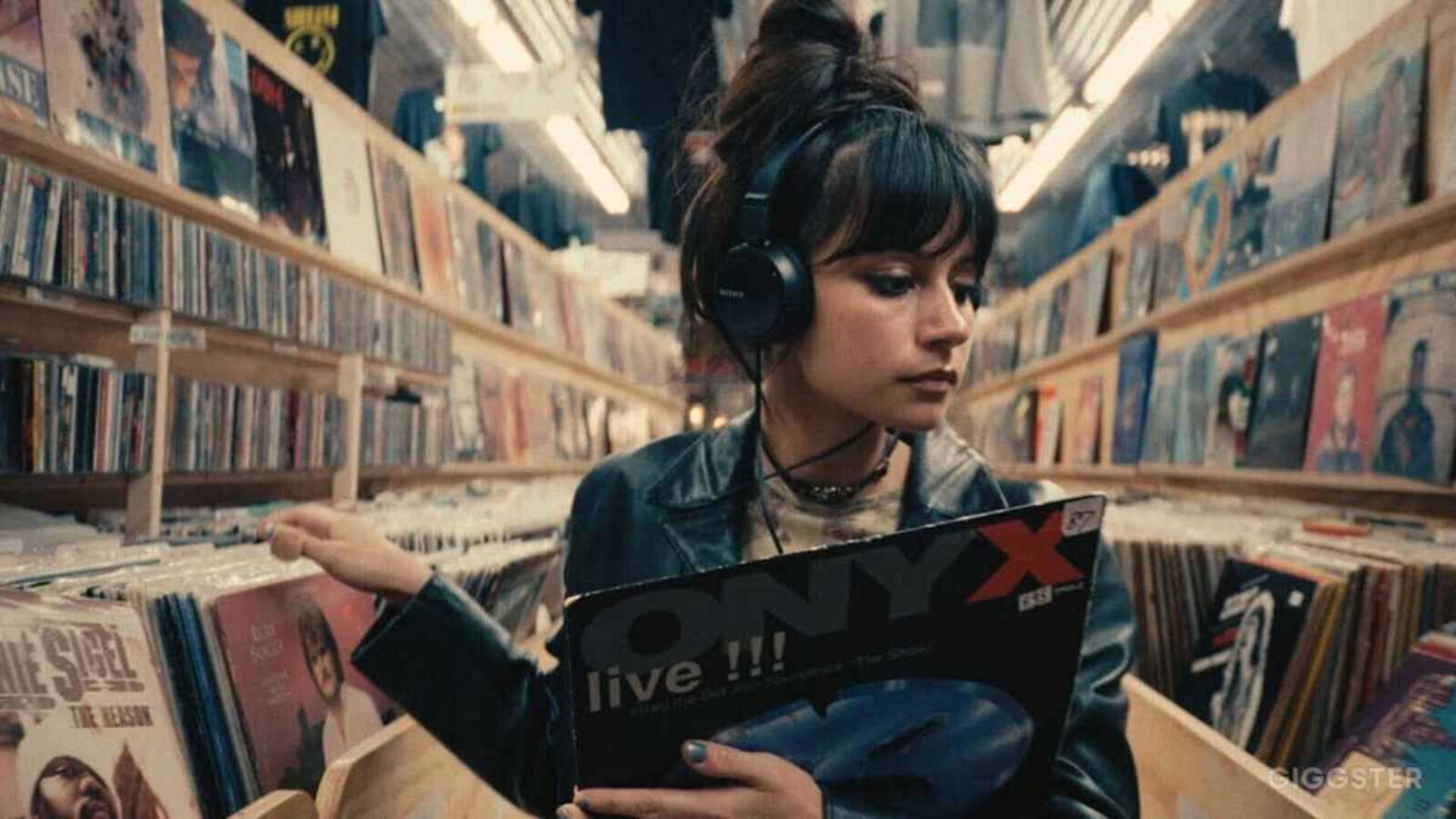 A young woman wearing headphones browses through vinyl records in a music shop aisle.