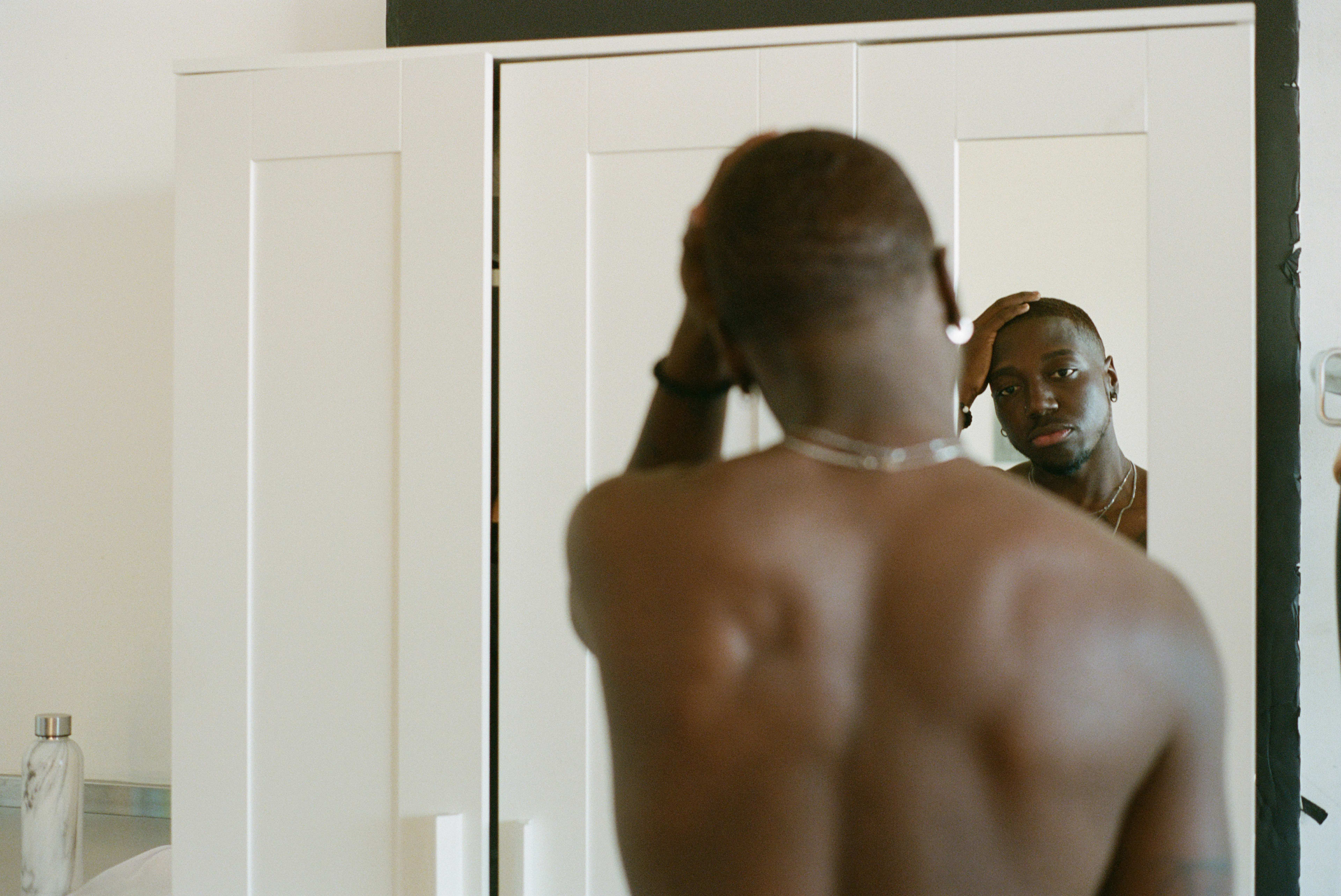 Una persona posando para una sesión de fotos minimalista en blanco mientras mira su reflejo en el espejo.