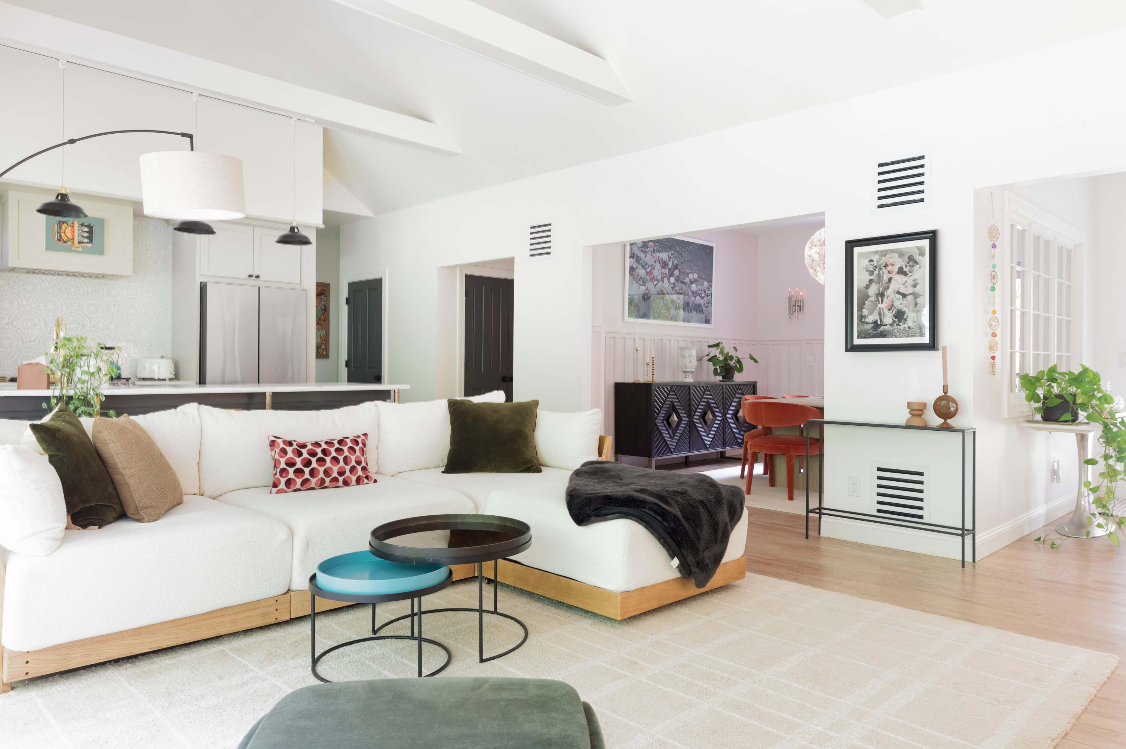 The image shows a modern living room with a sectional sofa, a coffee table, and an open layout leading to a dining area.