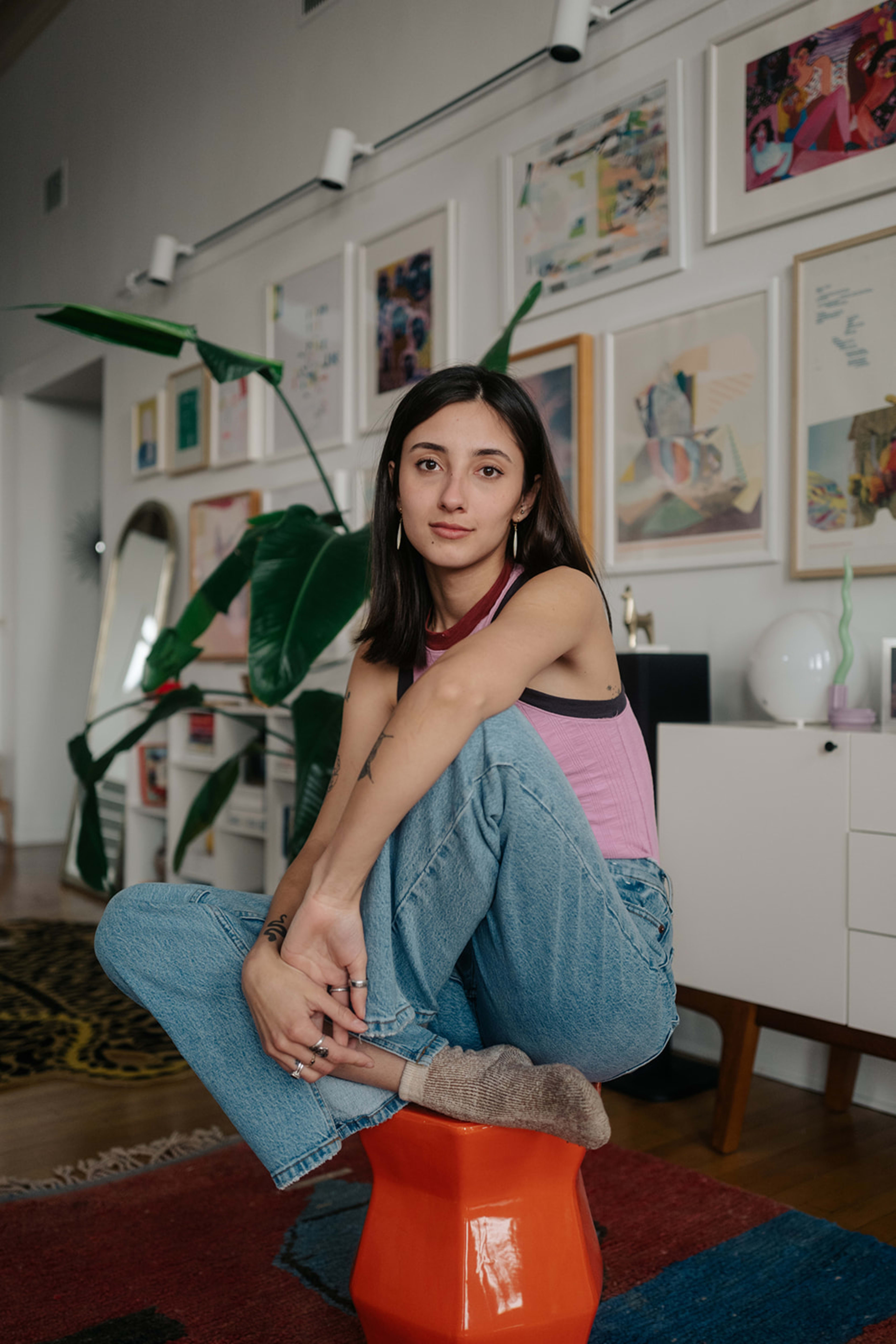 A woman posing for a 1990s fashion photo shoot by plant on the floor.