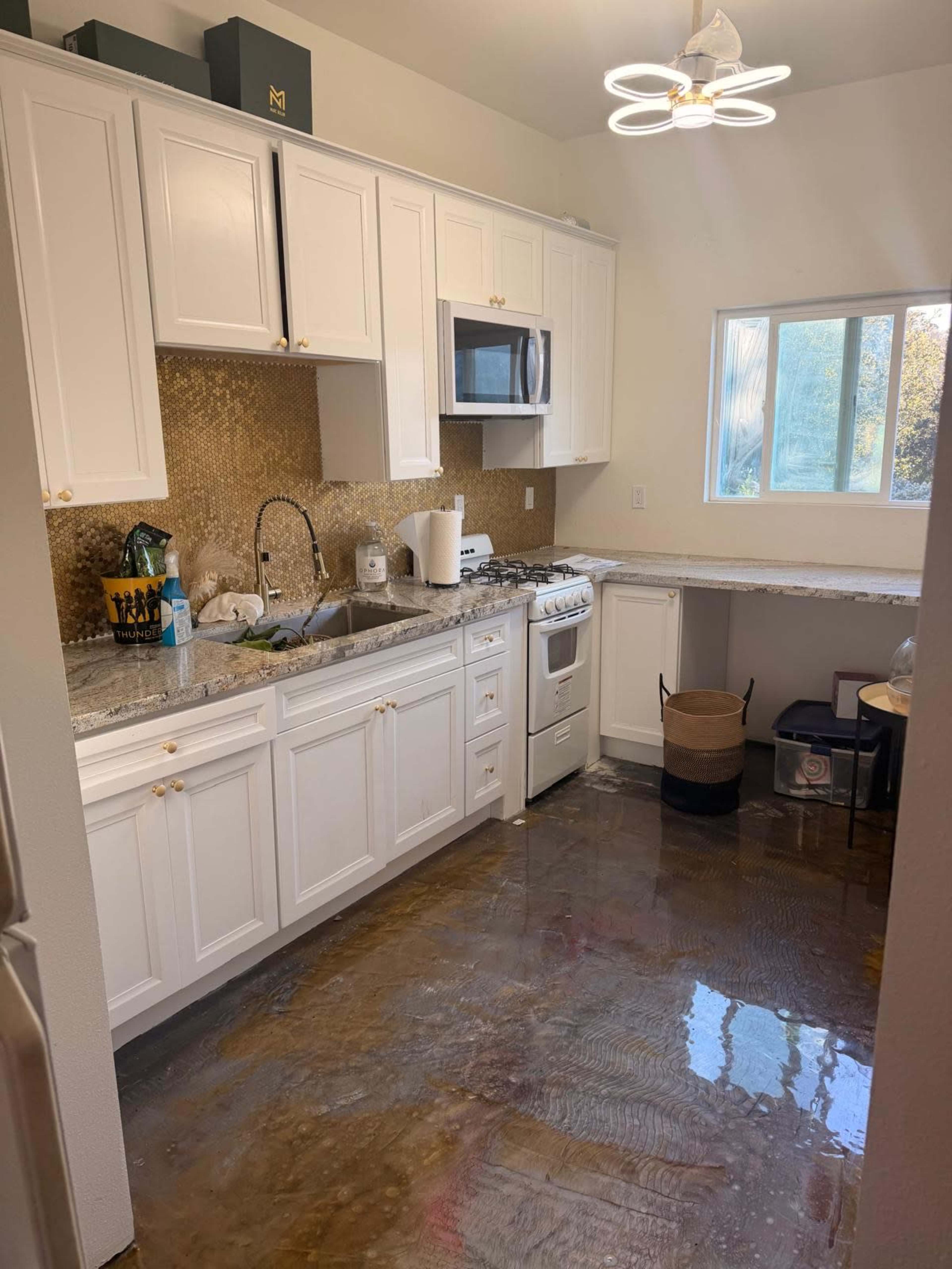 The image shows a modern kitchen with white cabinets, a stainless steel appliance setup, and a polished floor reflecting the overhead lighting.