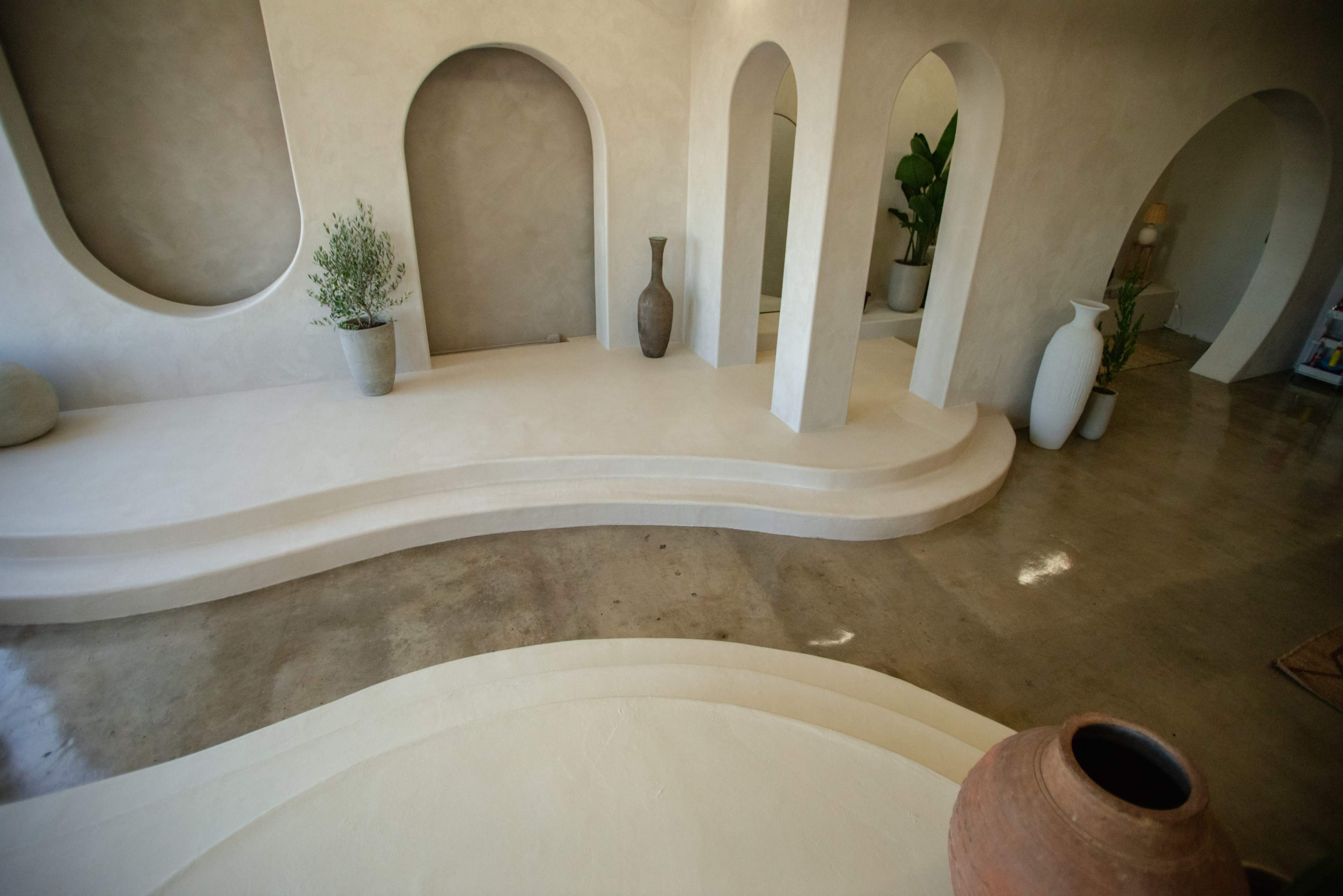 A minimalist interior space with curved steps, arched openings, and a combination of decorative vases and plants.