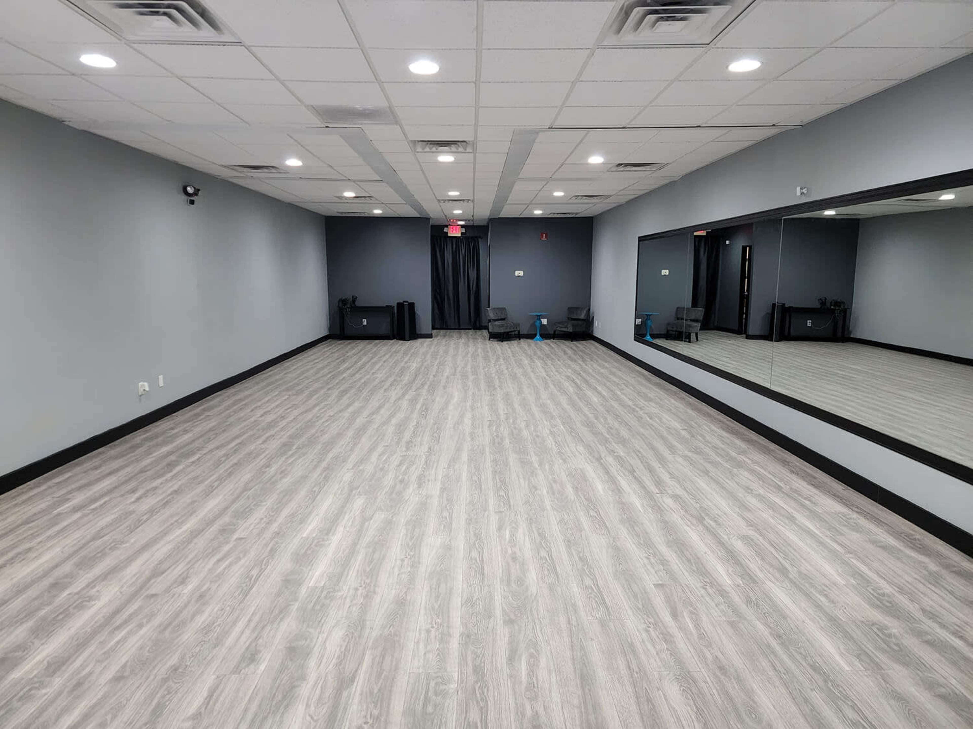 A spacious, empty room with gray walls, light wood flooring, and a large mirror along one side.