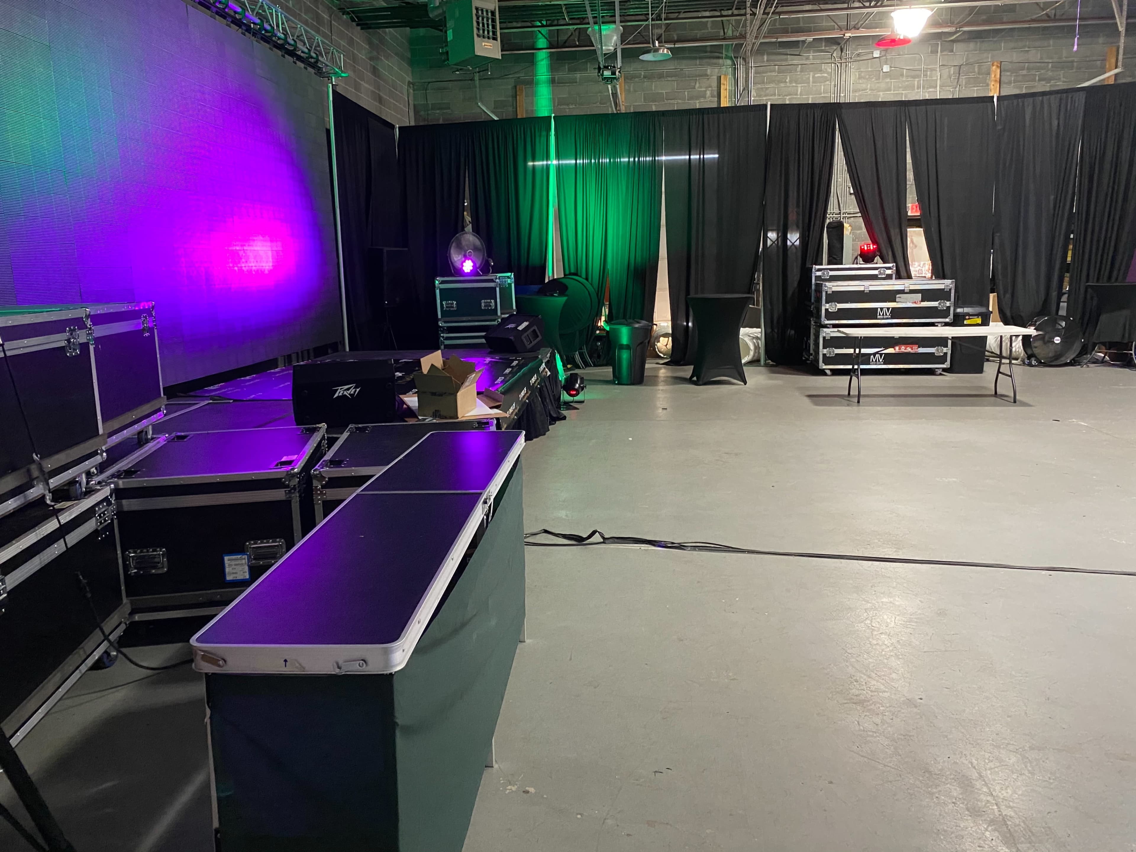 A spacious venue with black drapes, stage lighting, and equipment cases organized along the floor.
