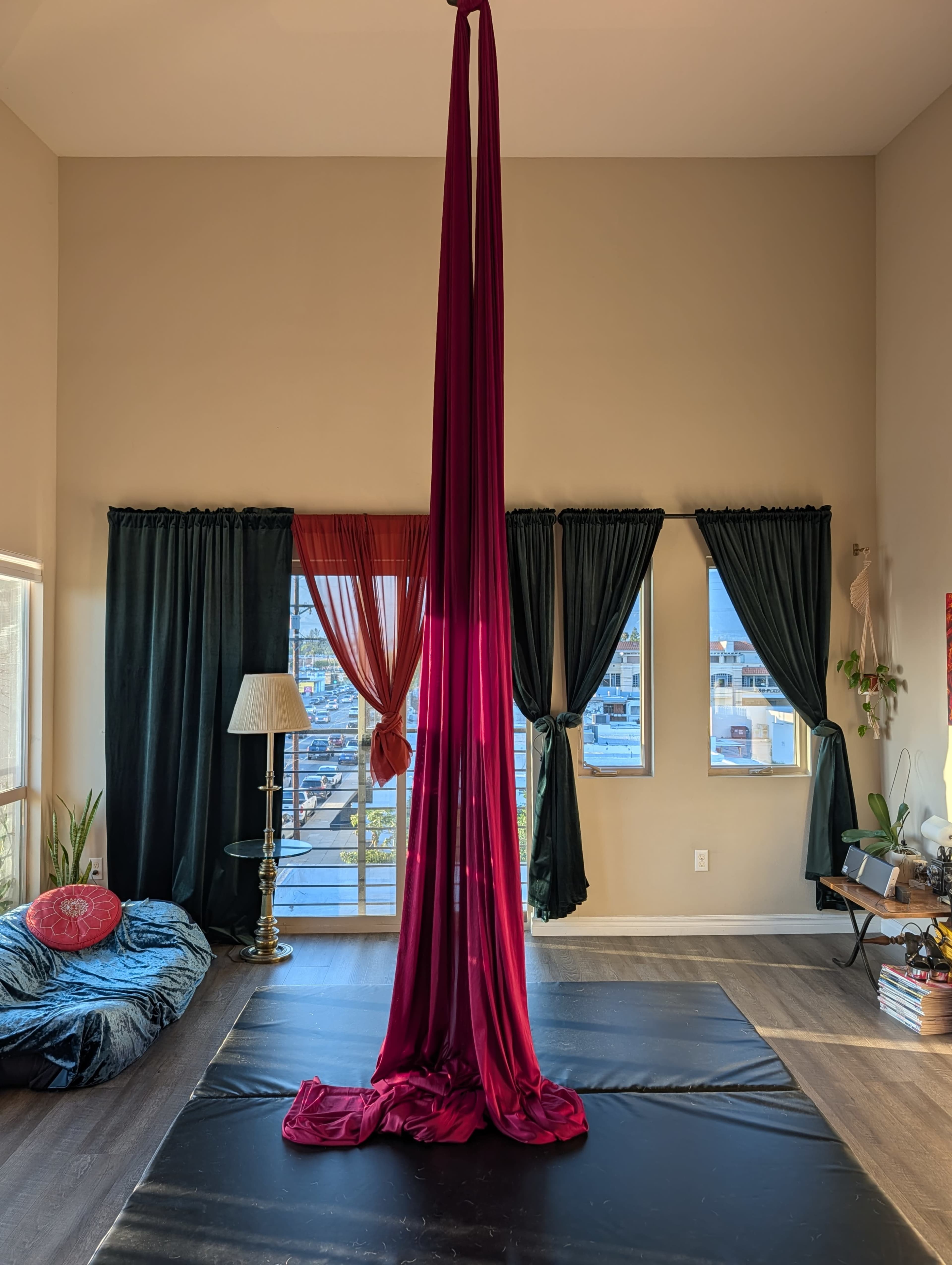 A long red silk aerial fabric hangs from the ceiling in a spacious room with large windows and dark curtains.