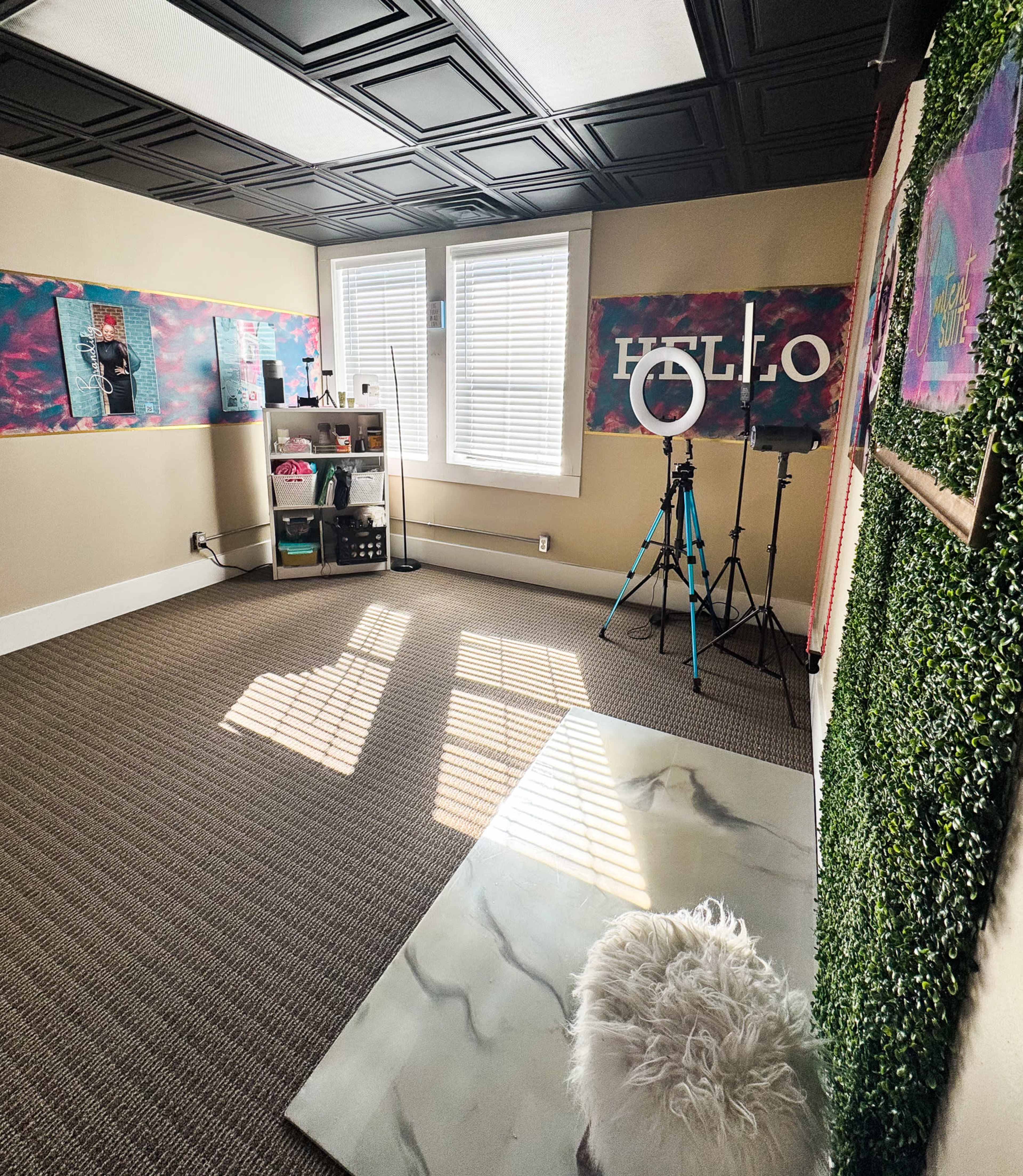 The image shows a bright, empty room decorated with colorful wall art, a ring light, and a shelf filled with various items.