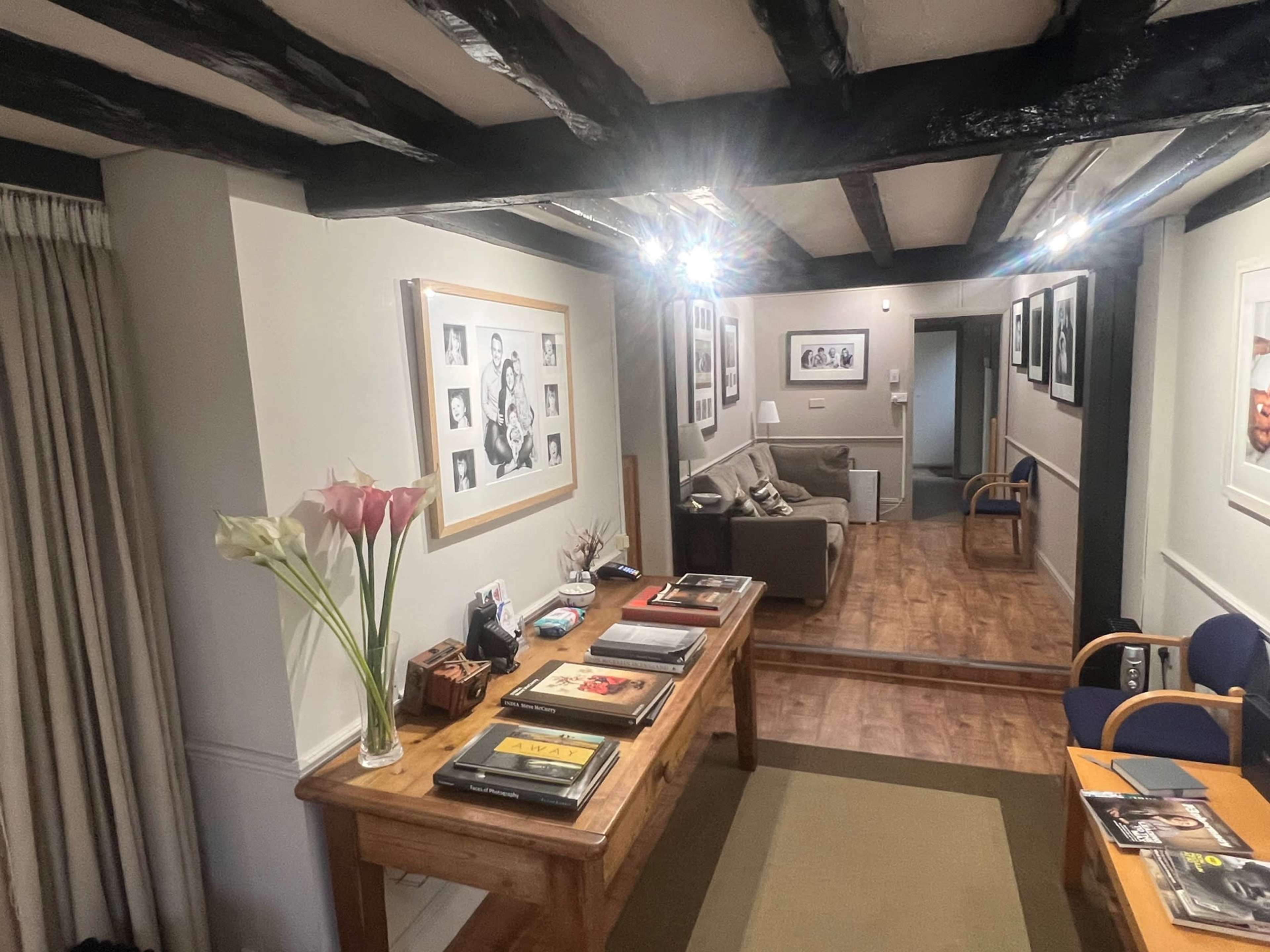 A reception area with a wooden table displaying magazines, flanked by seating areas and framed photographs on the walls.