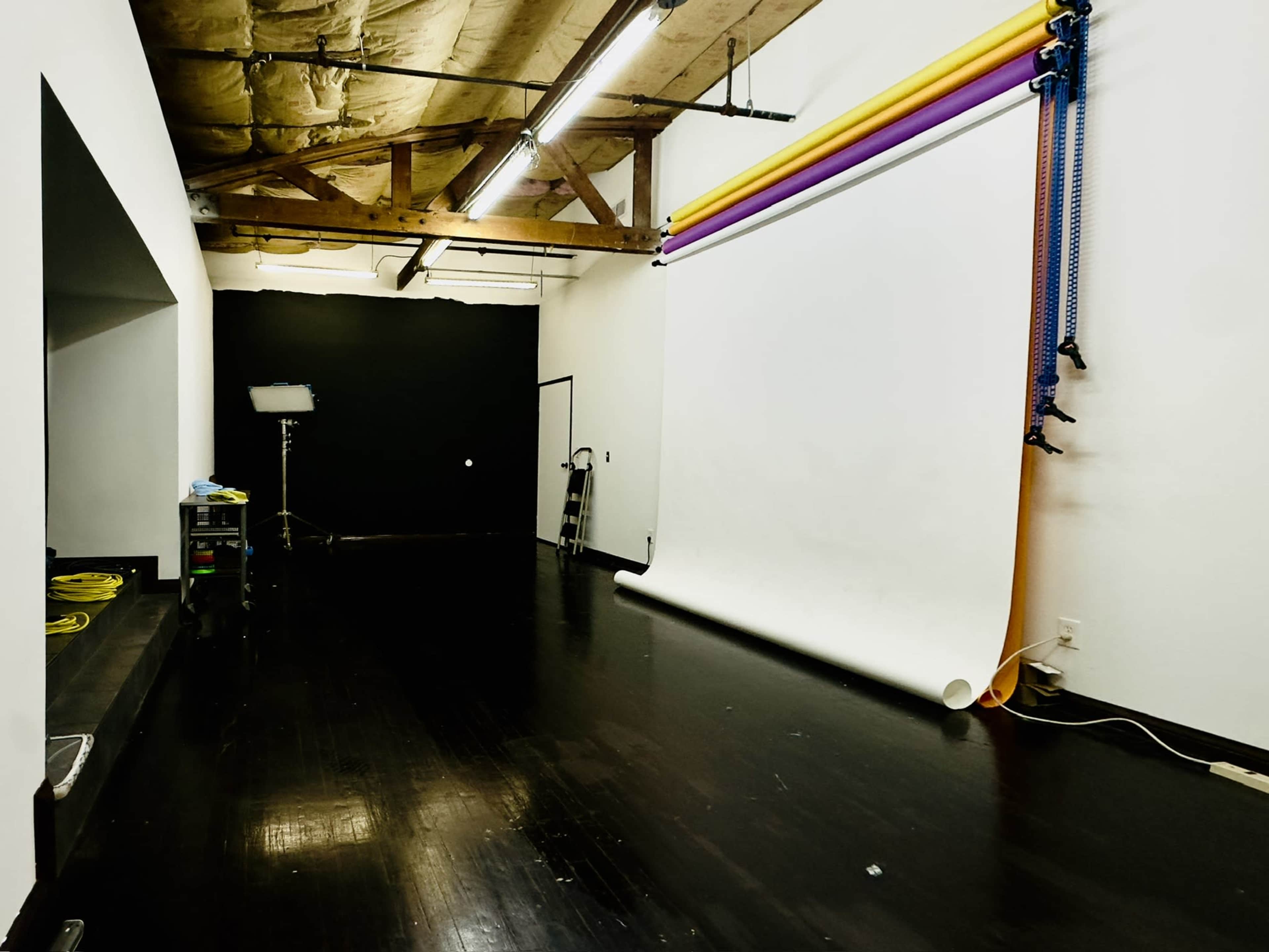 A photography studio with a seamless backdrop, roll-up support, and a black wall.