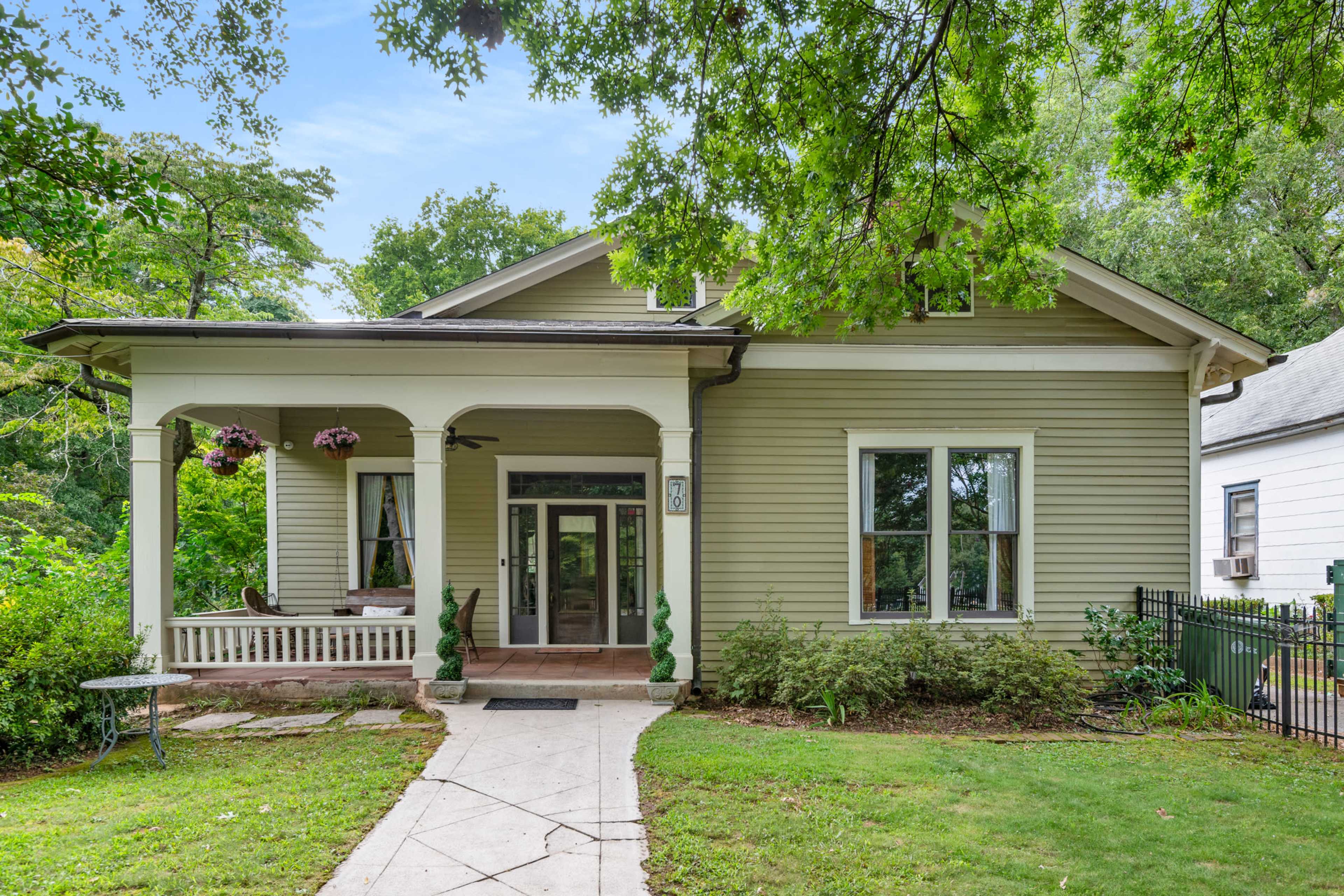 The image shows a light-colored, single-story house with a wide front porch and a landscaped yard.