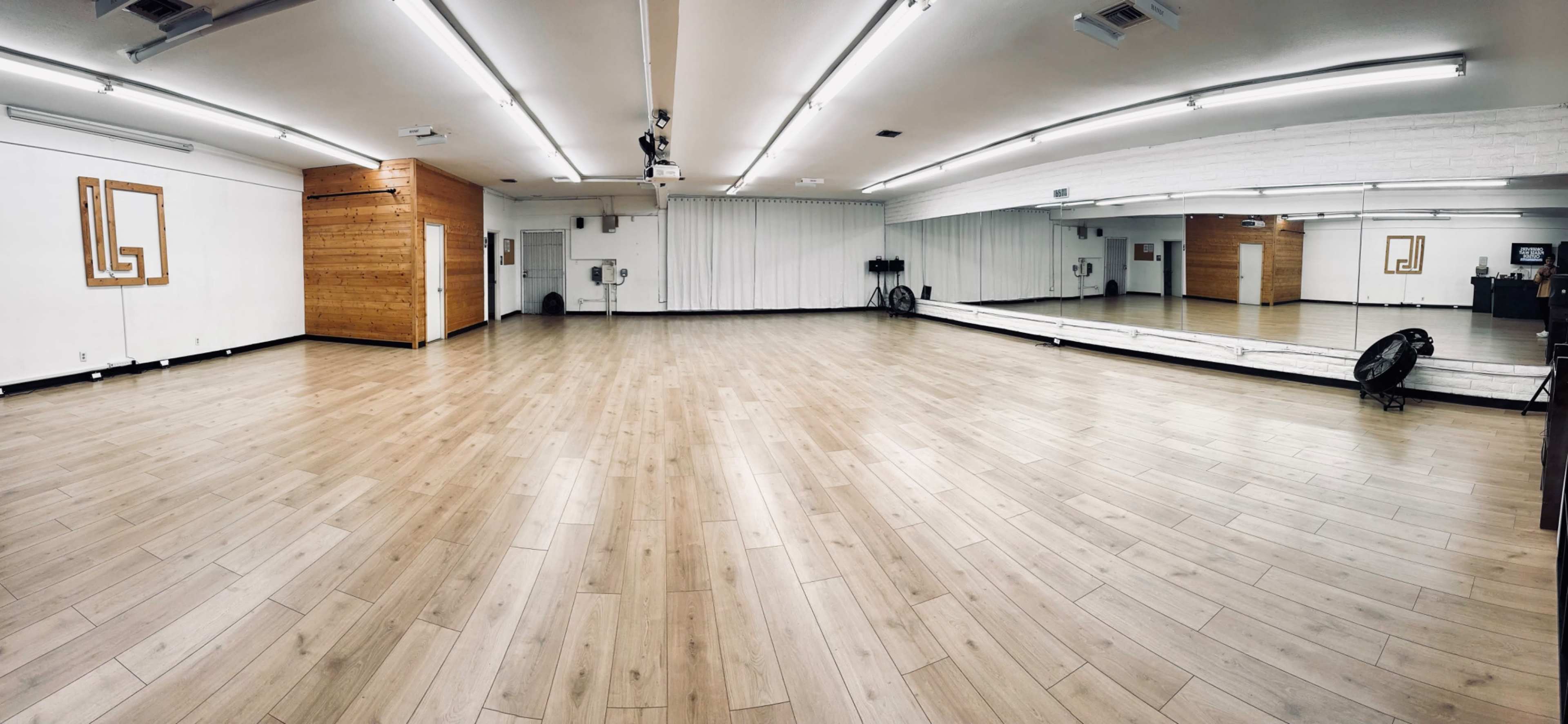 The image shows a spacious wooden floor dance studio with mirrored walls and ample ceiling lights.