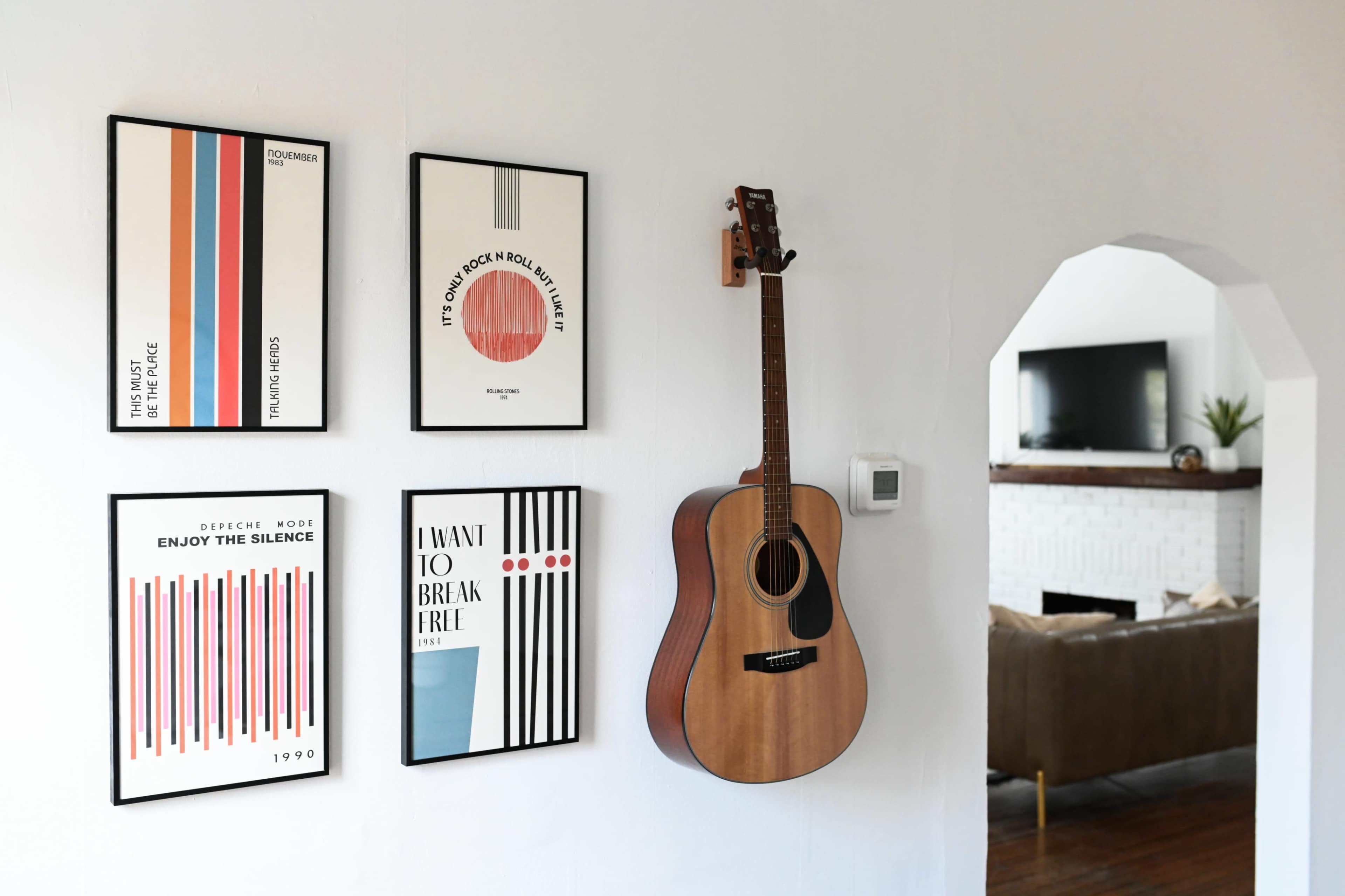 A wooden acoustic guitar hangs on a wall alongside several framed posters featuring geometric designs and text.