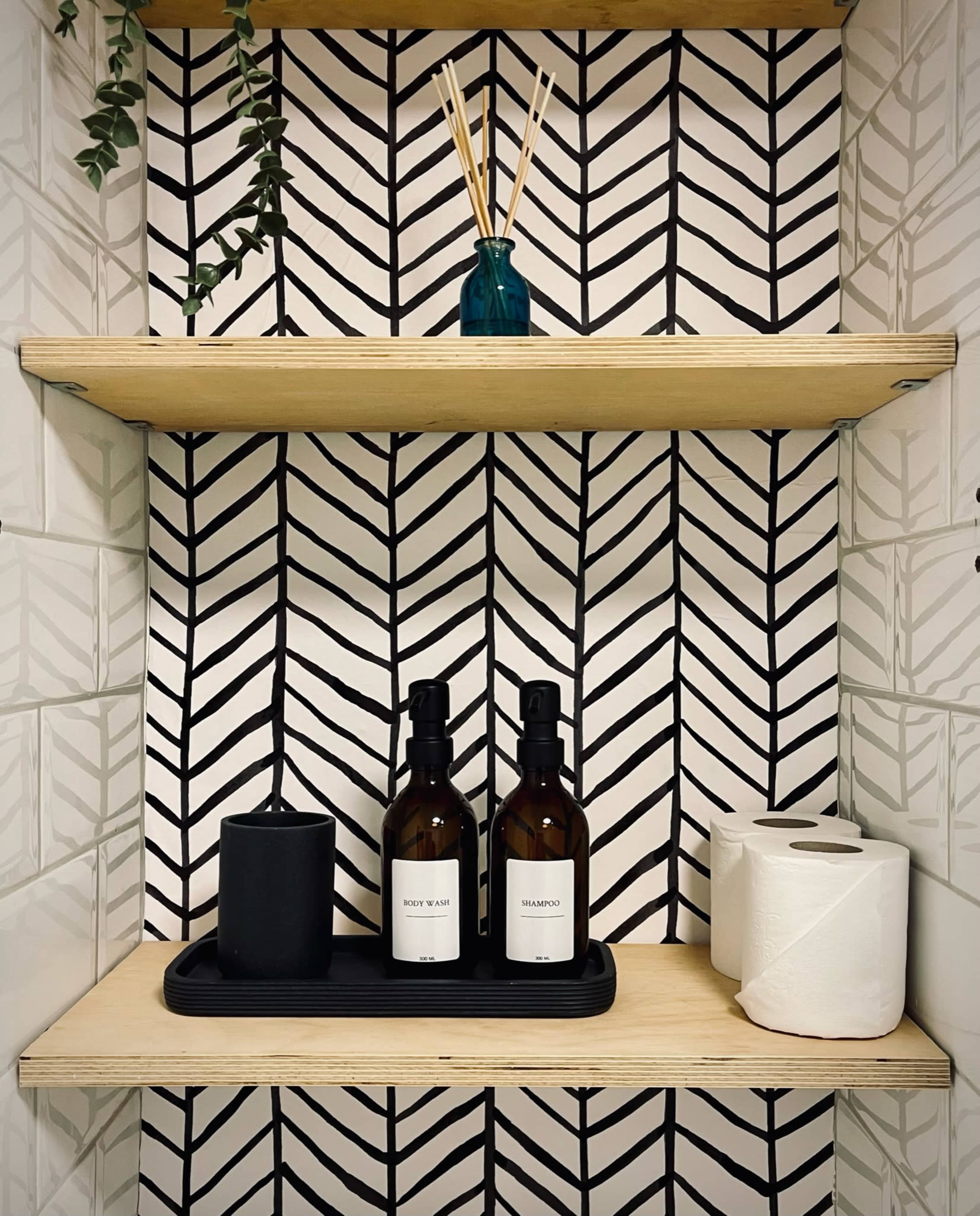 A wooden shelf displays various personal care products and decorative items against a patterned black and white tiled background.