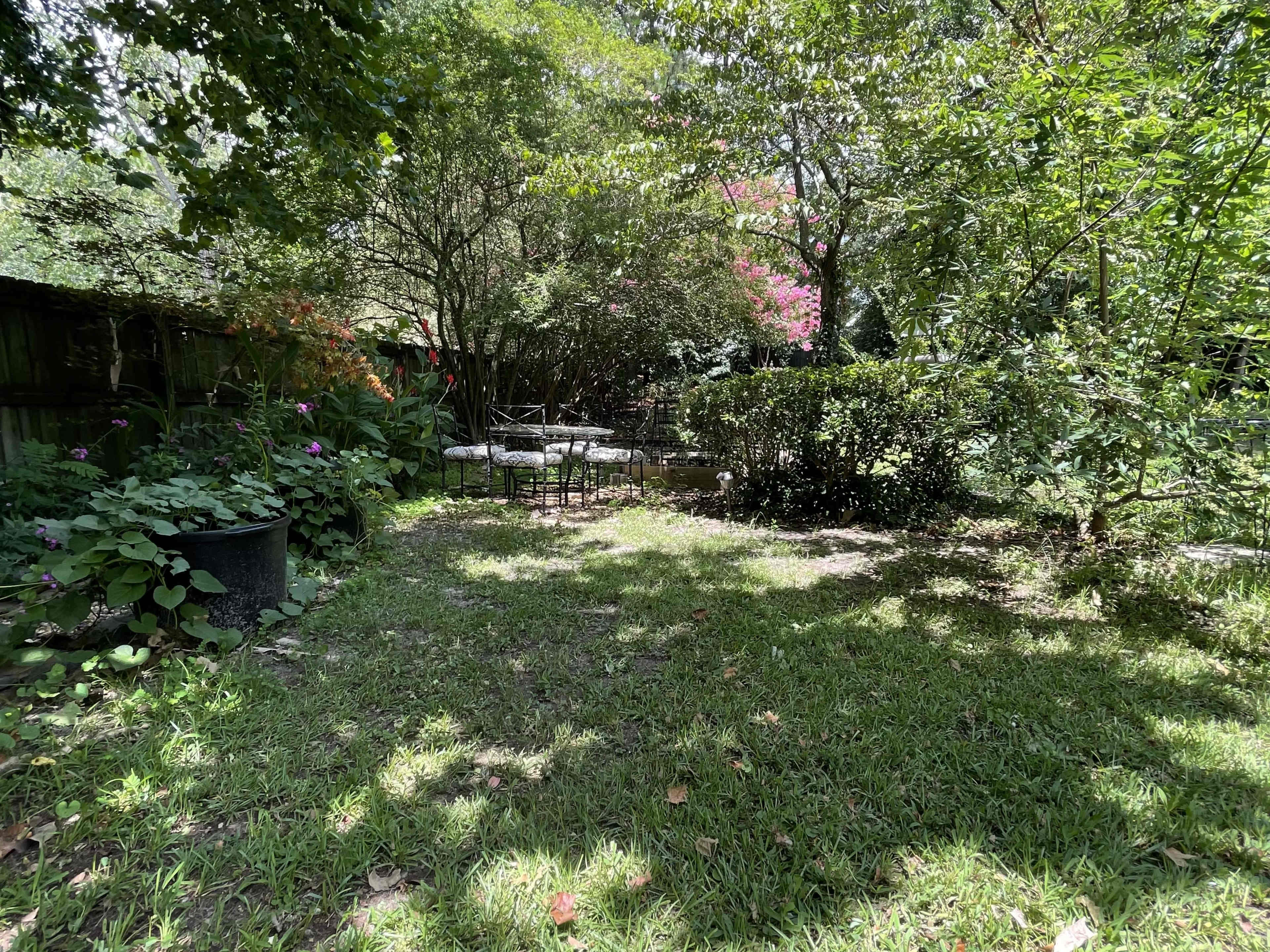 The image shows a green garden space with a small seating area surrounded by trees and shrubs.
