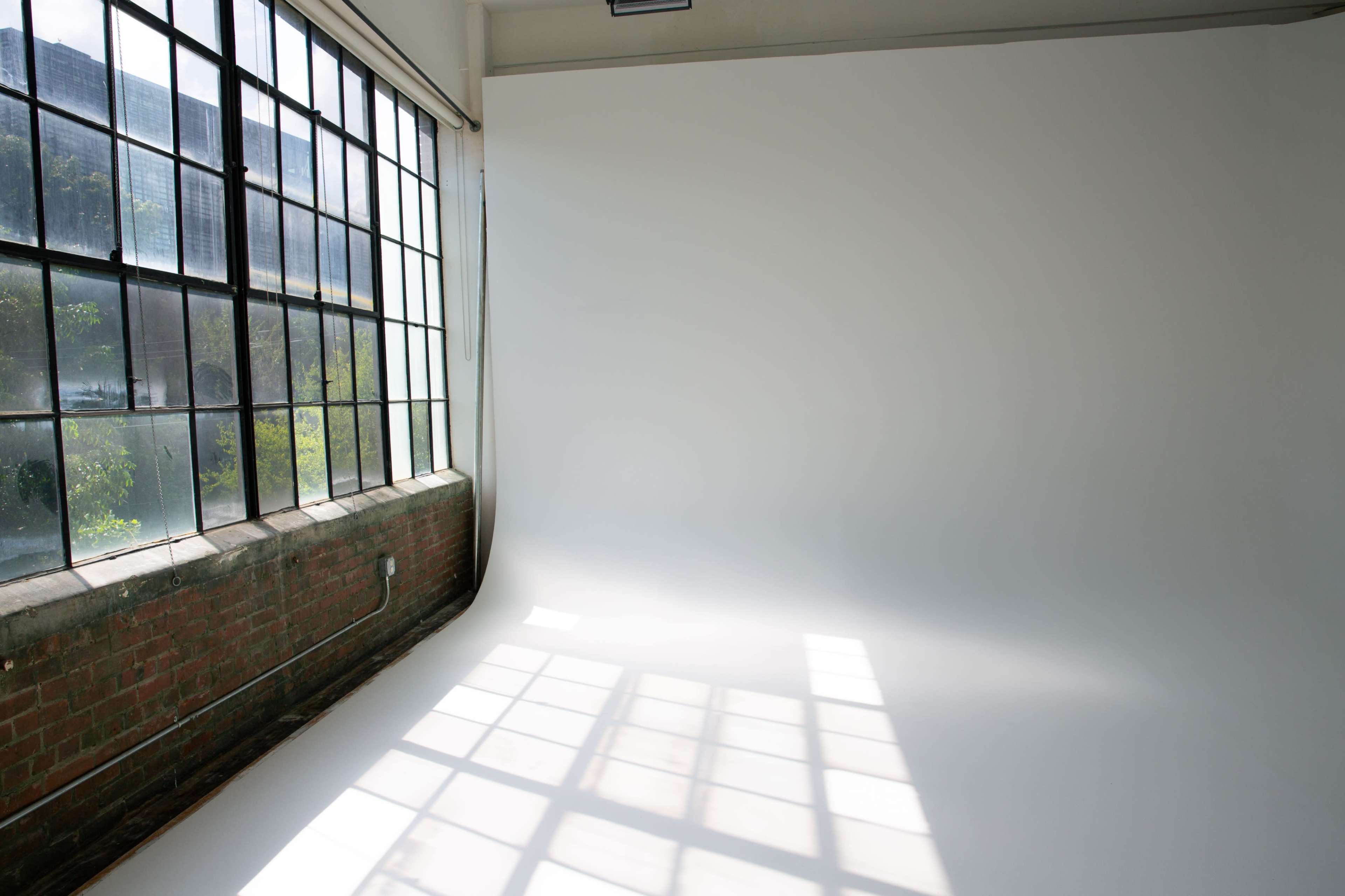 The image shows a spacious, bright studio with large windows and a smooth white backdrop.