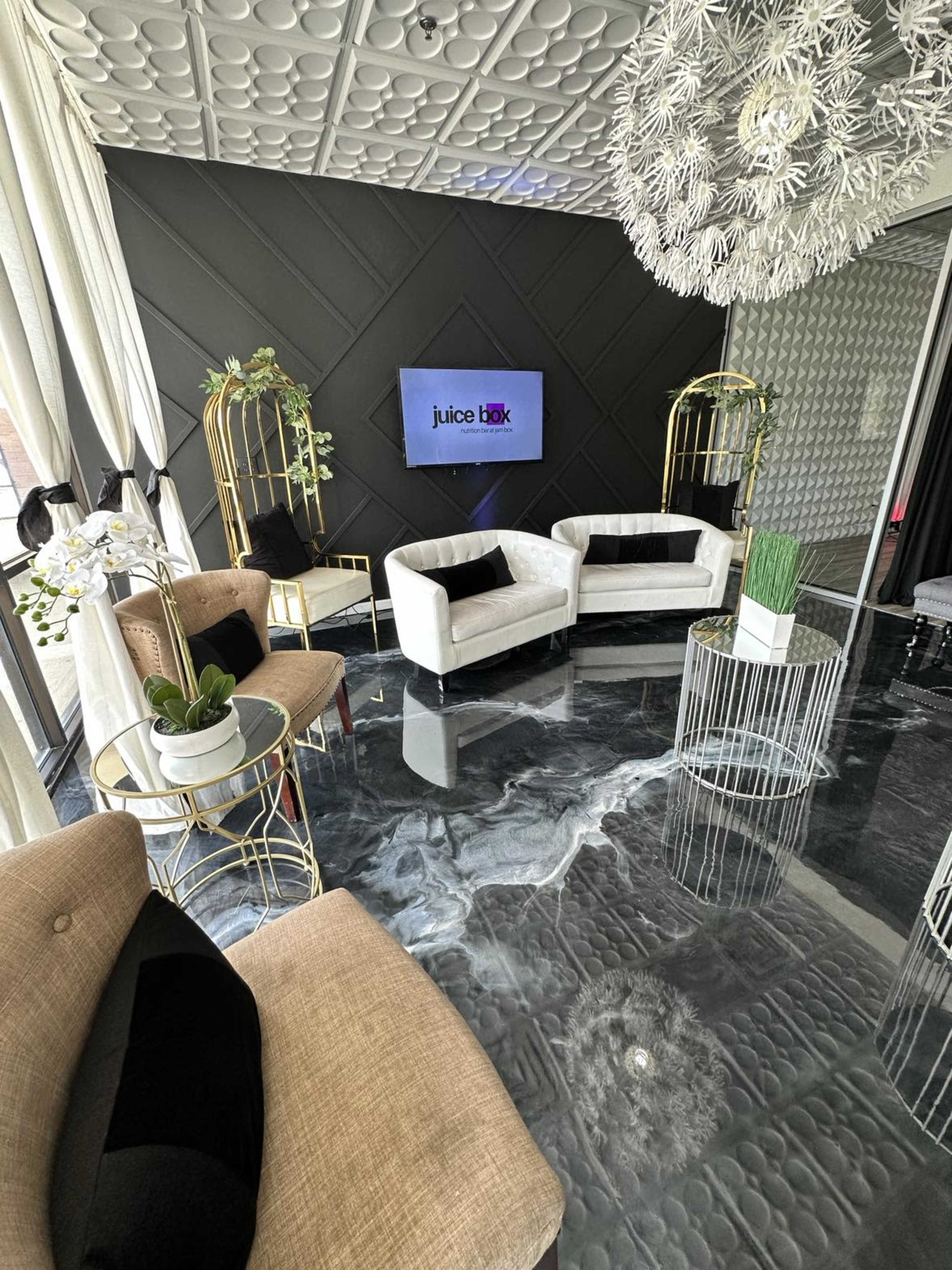 A modern, stylish lounge area featuring white sofas, elegant tables, and decorative plants, with a television displaying the "juice lab" logo on a black wall.