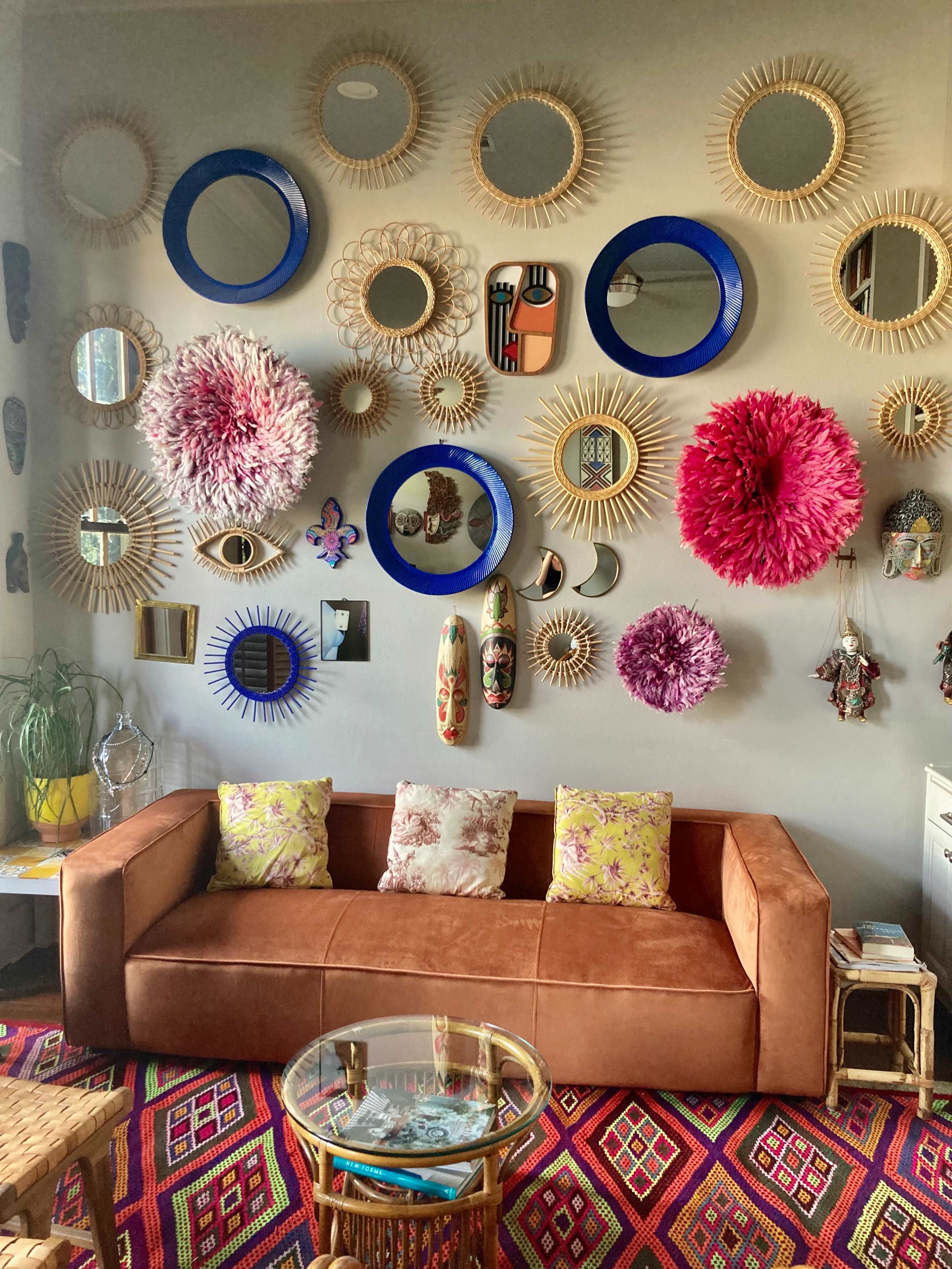 The image shows a living room with a brown couch and a wall adorned with various decorative mirrors and colorful wall art.