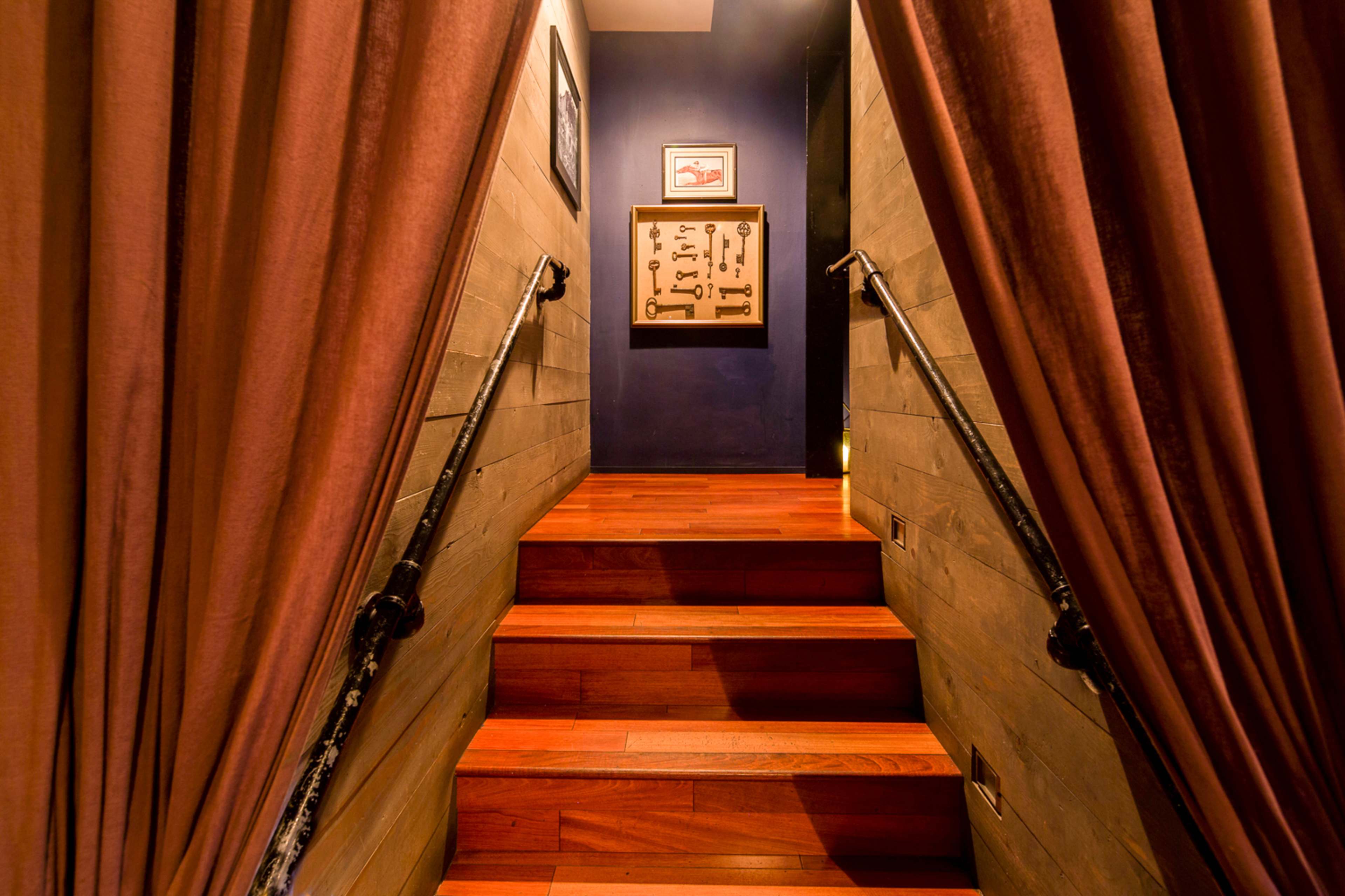 A staircase leads upward through a pair of curtains, with a framed display of keys on the wall at the top.