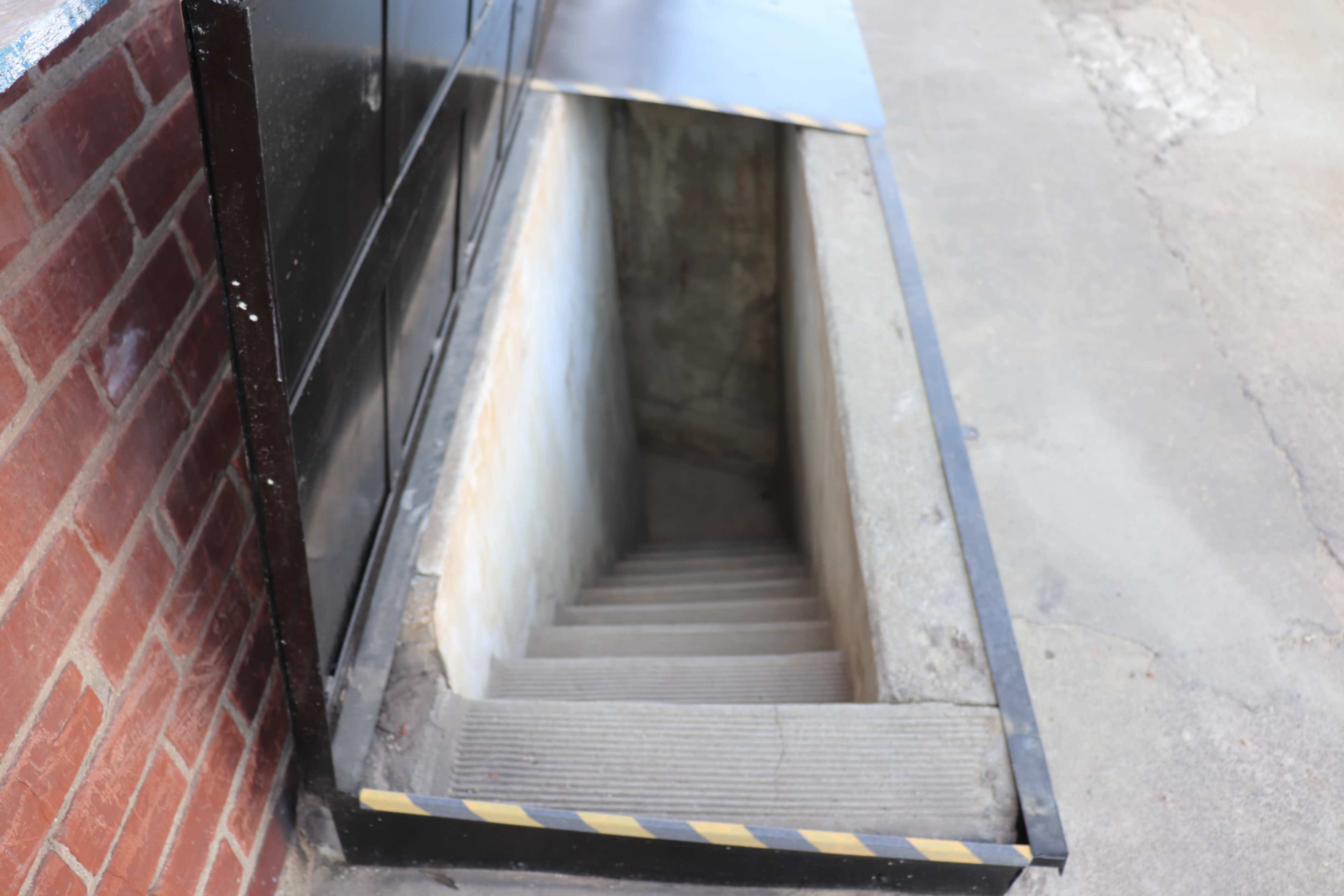 A concrete stairway leads down into a basement through a narrow, recessed opening beside a brick wall.