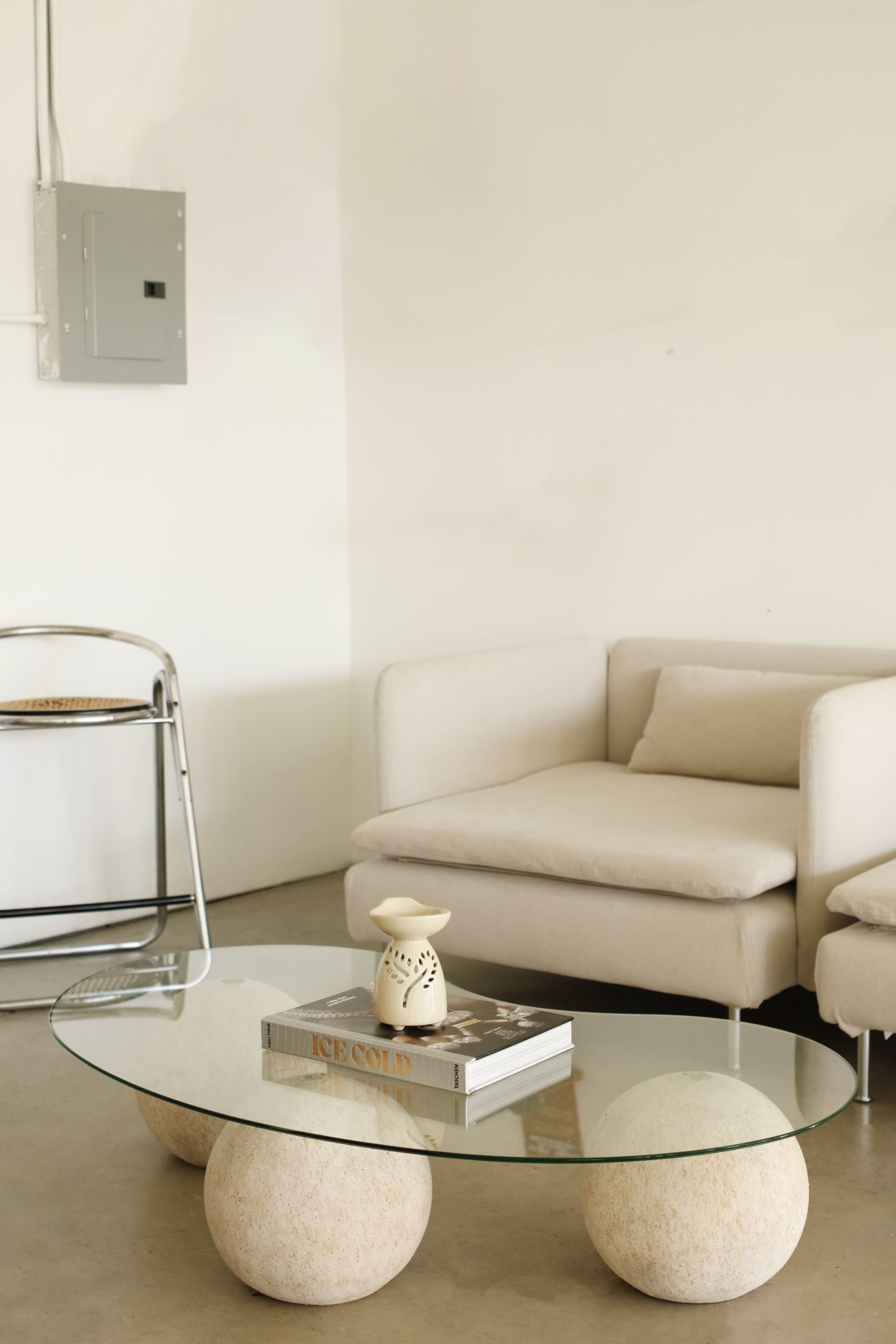A modern living room with a beige sofa, a glass coffee table supported by rounded stone bases, and a small decorative item on the table.