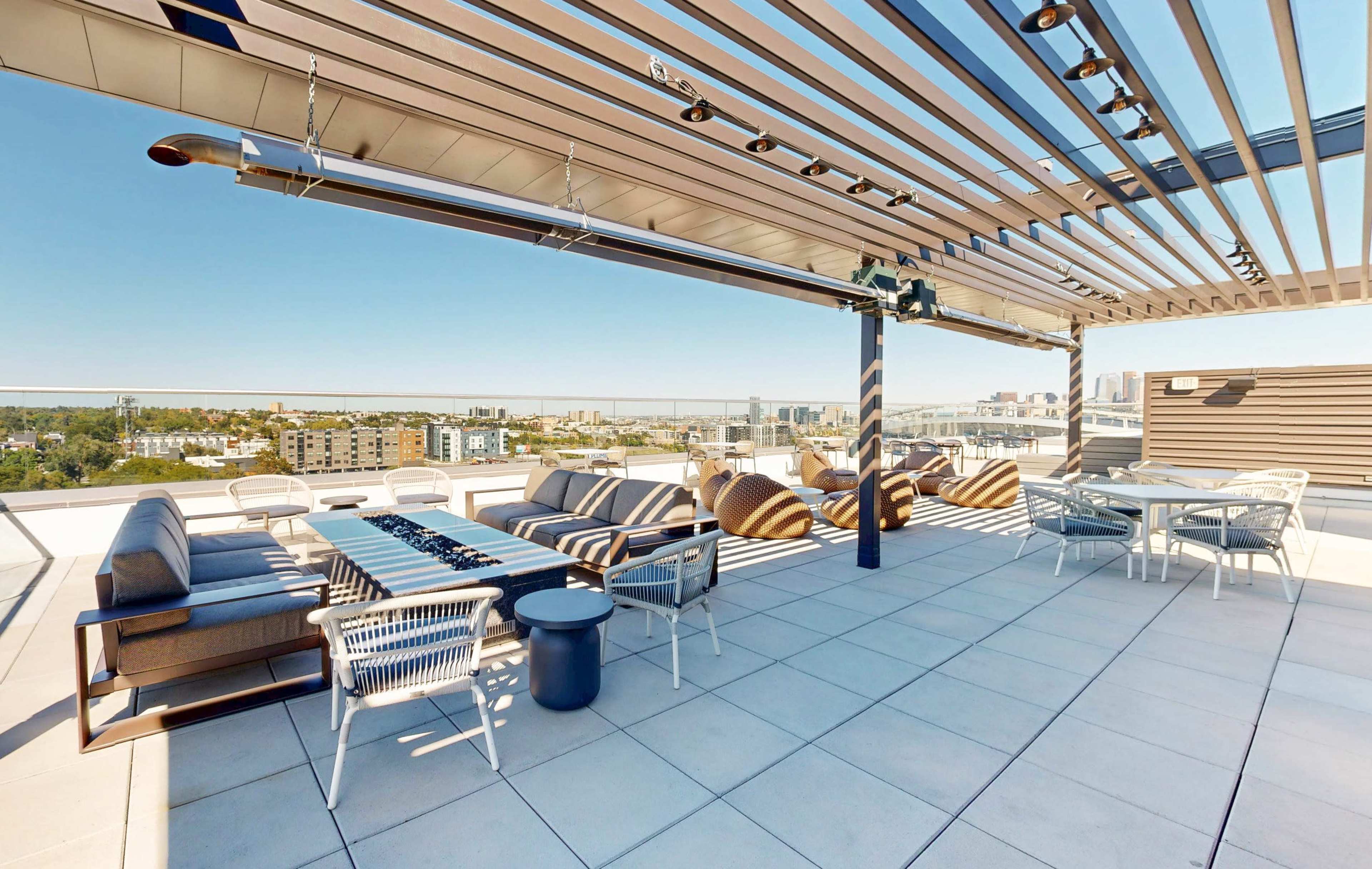 The image shows a rooftop terrace featuring several seating areas with sofas, armchairs, and a dining table, all overlooking a cityscape.