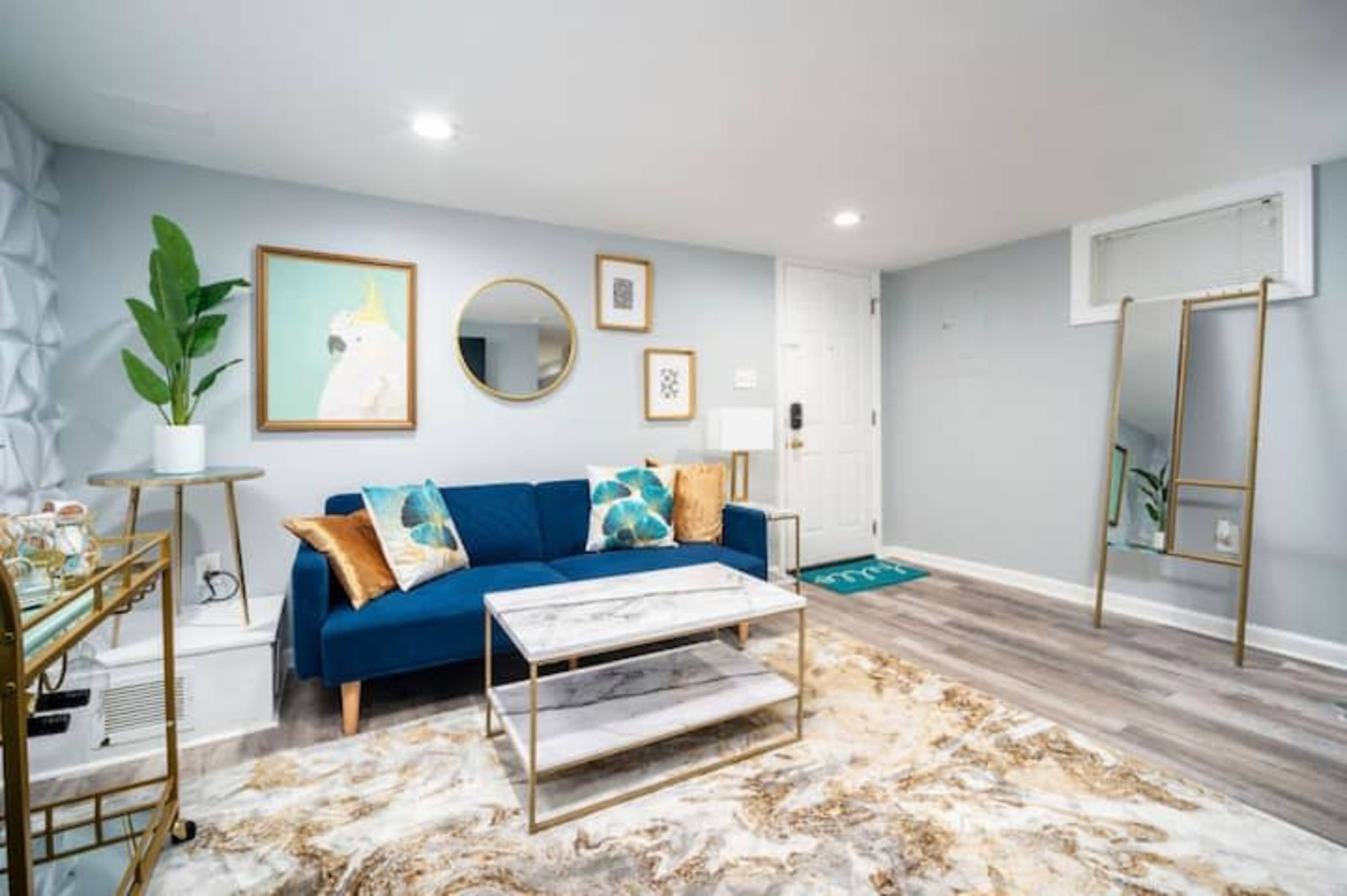 A modern living space with a blue sofa, a marble coffee table, decorative artwork on the walls, and a door leading outside.