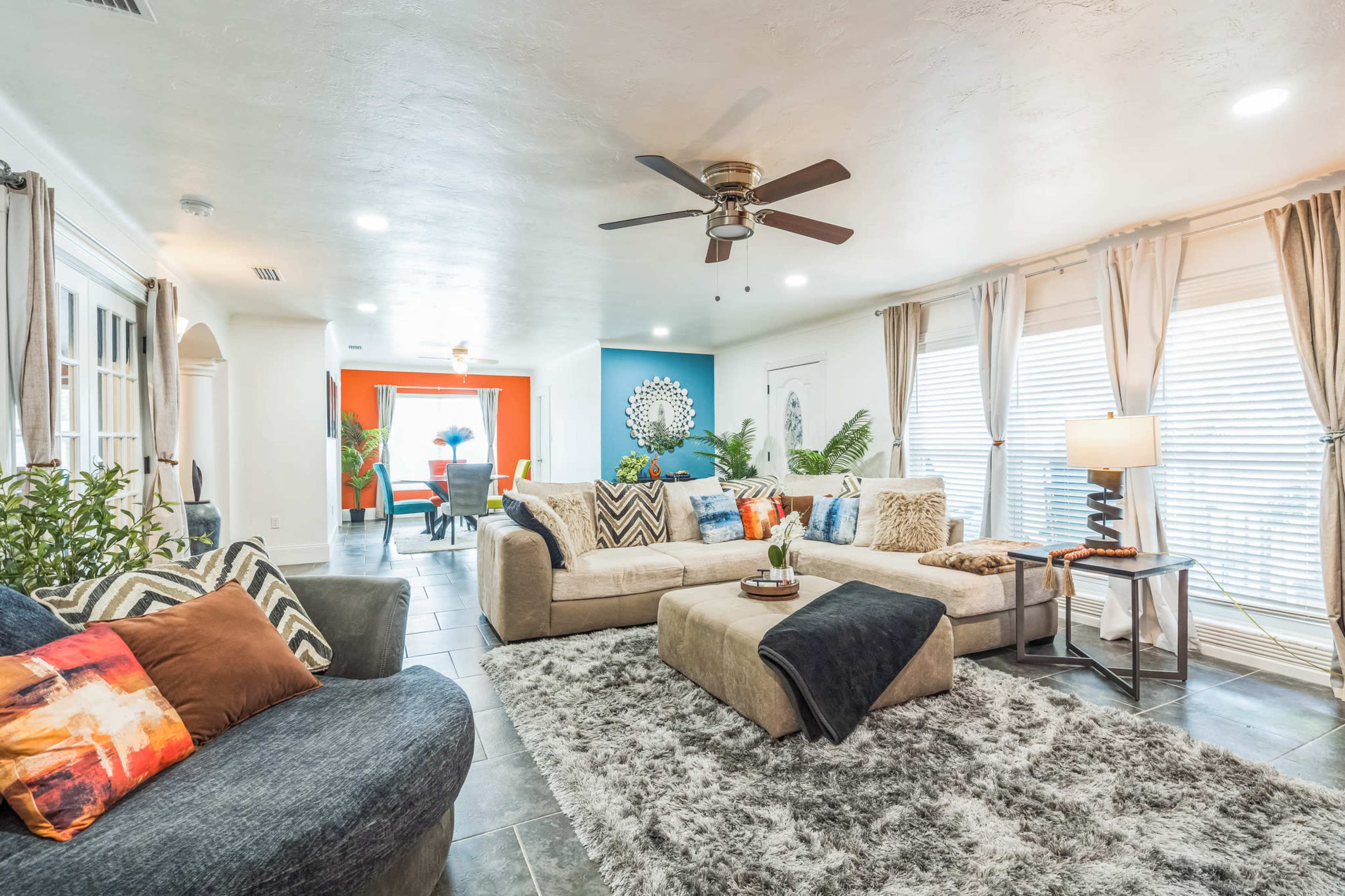 A spacious living room features a sectional sofa, a coffee table, and decorative plants, with light-colored walls and a blue accent wall.