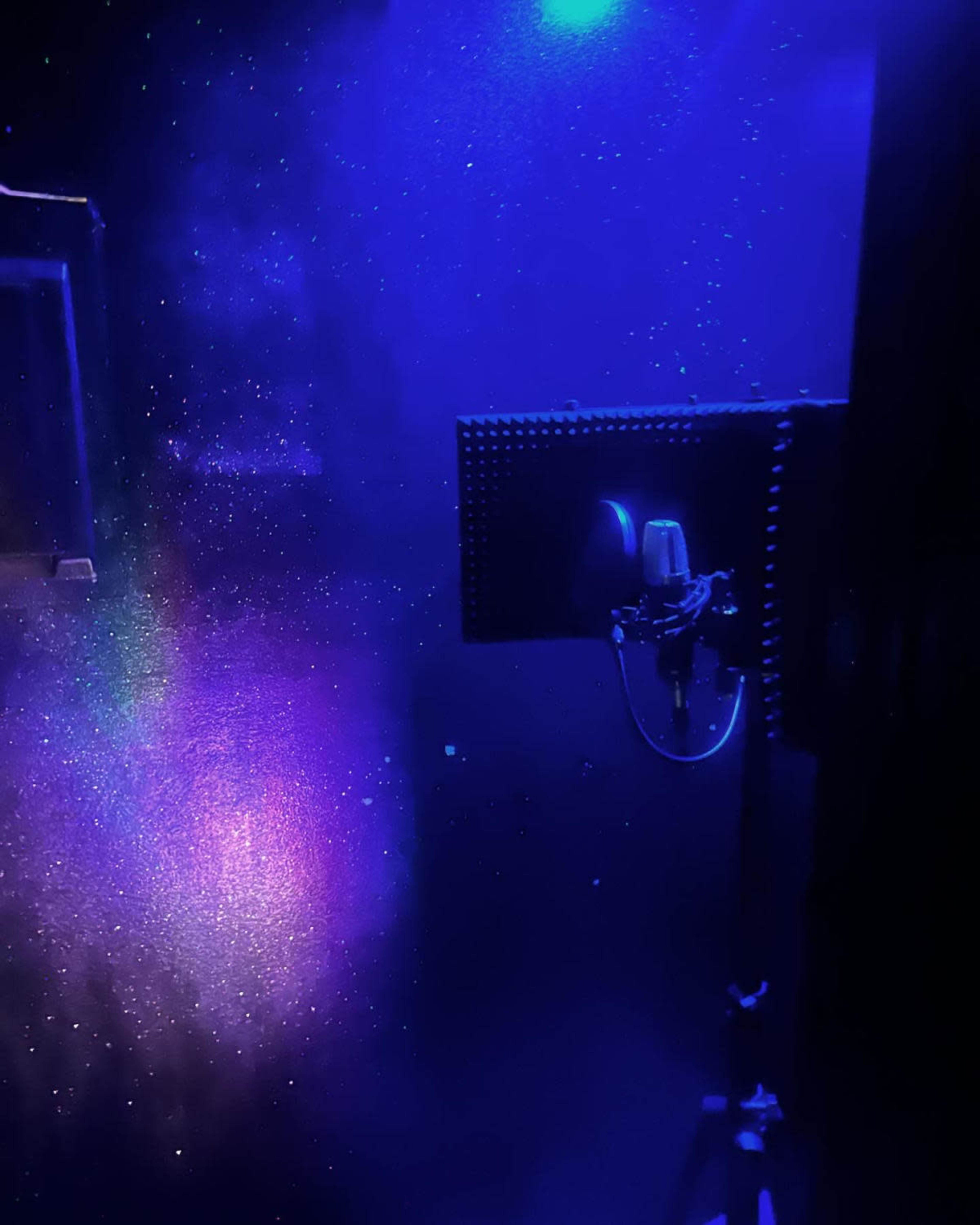 A microphone is positioned in a dimly lit room with a speckled, star-like background.