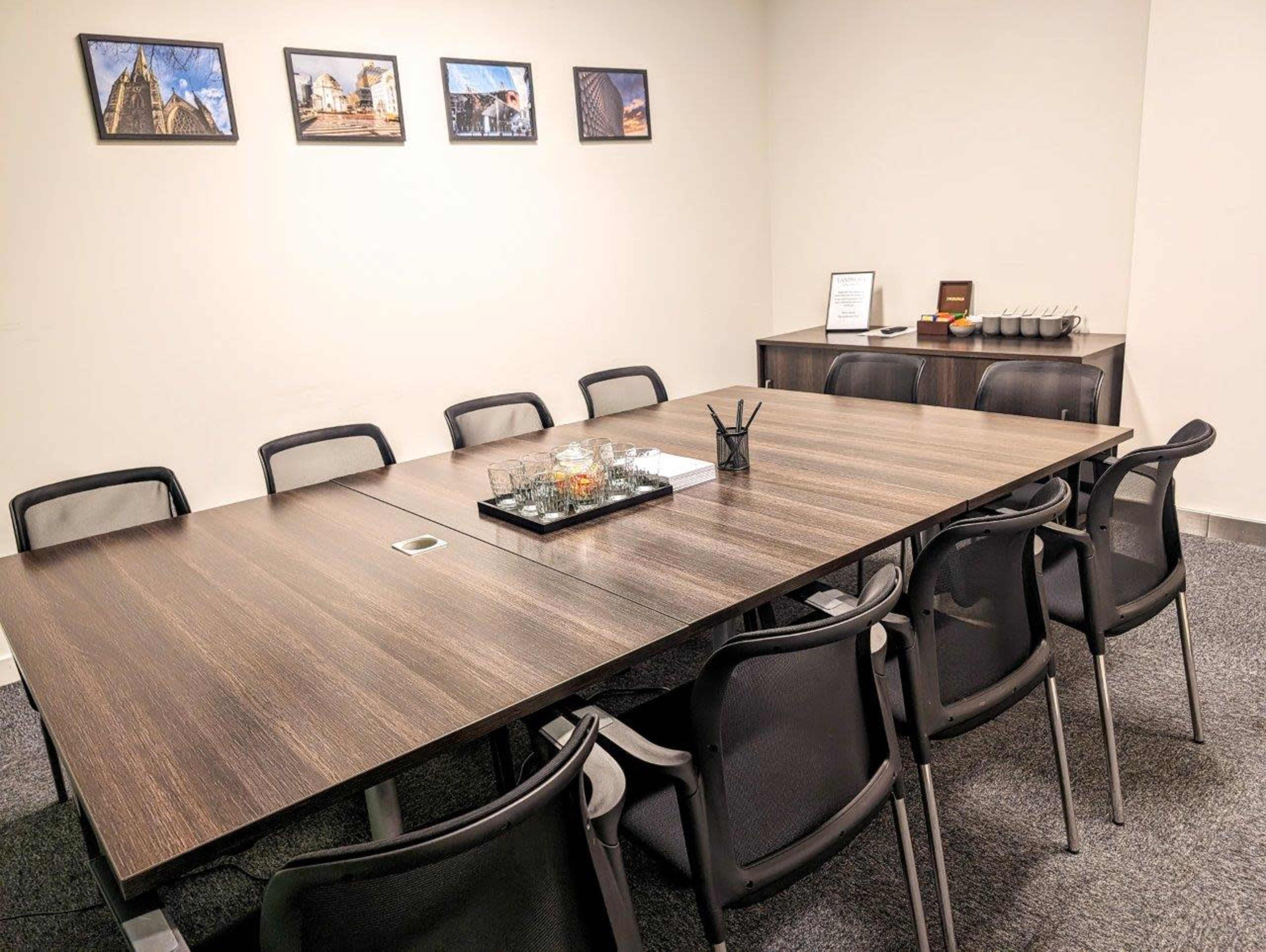 A large conference room features a rectangular wooden table surrounded by black chairs, with framed photographs on the wall and a side cabinet.