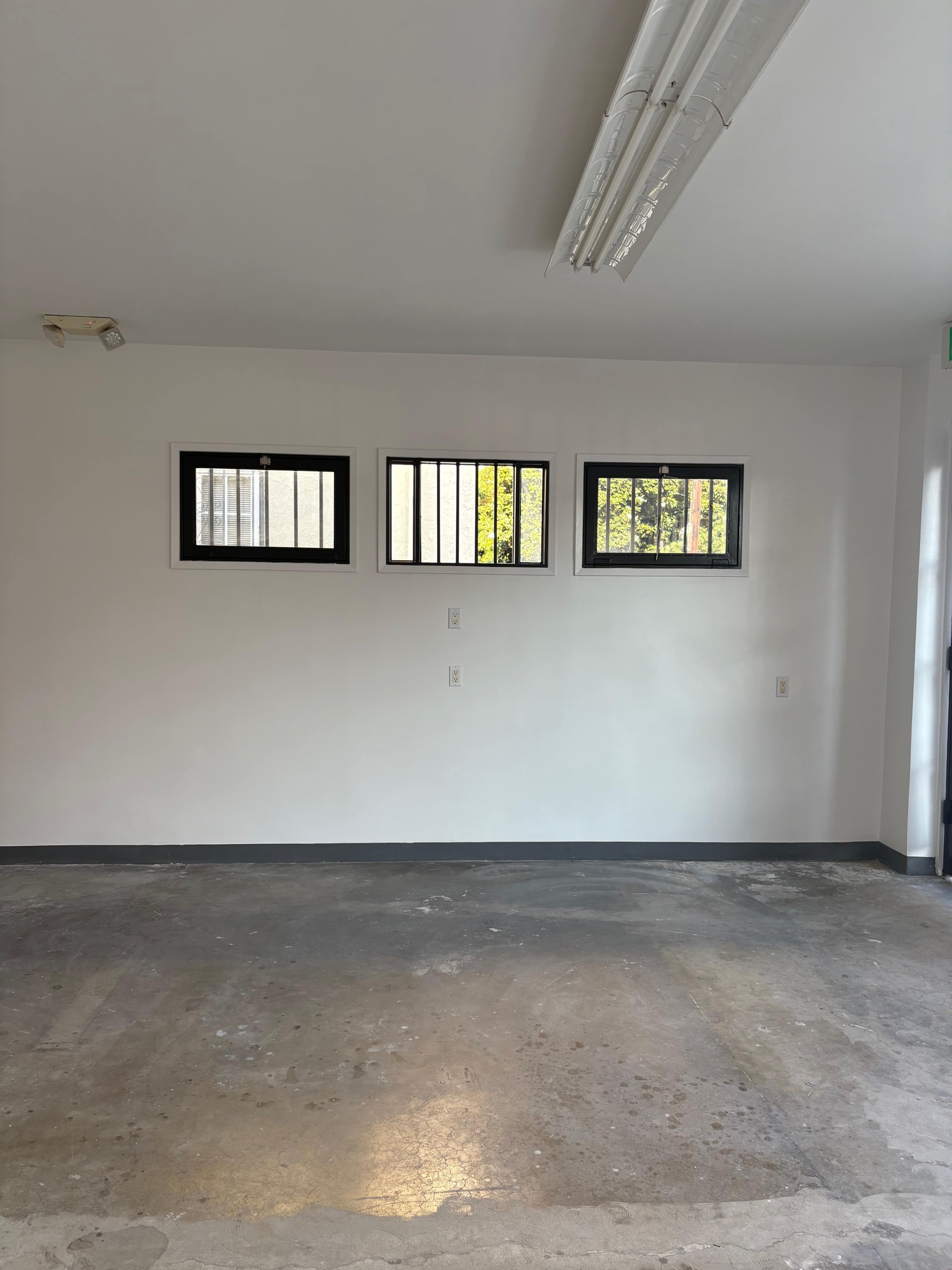 The image shows a bare interior of a room with three barred windows and a concrete floor.