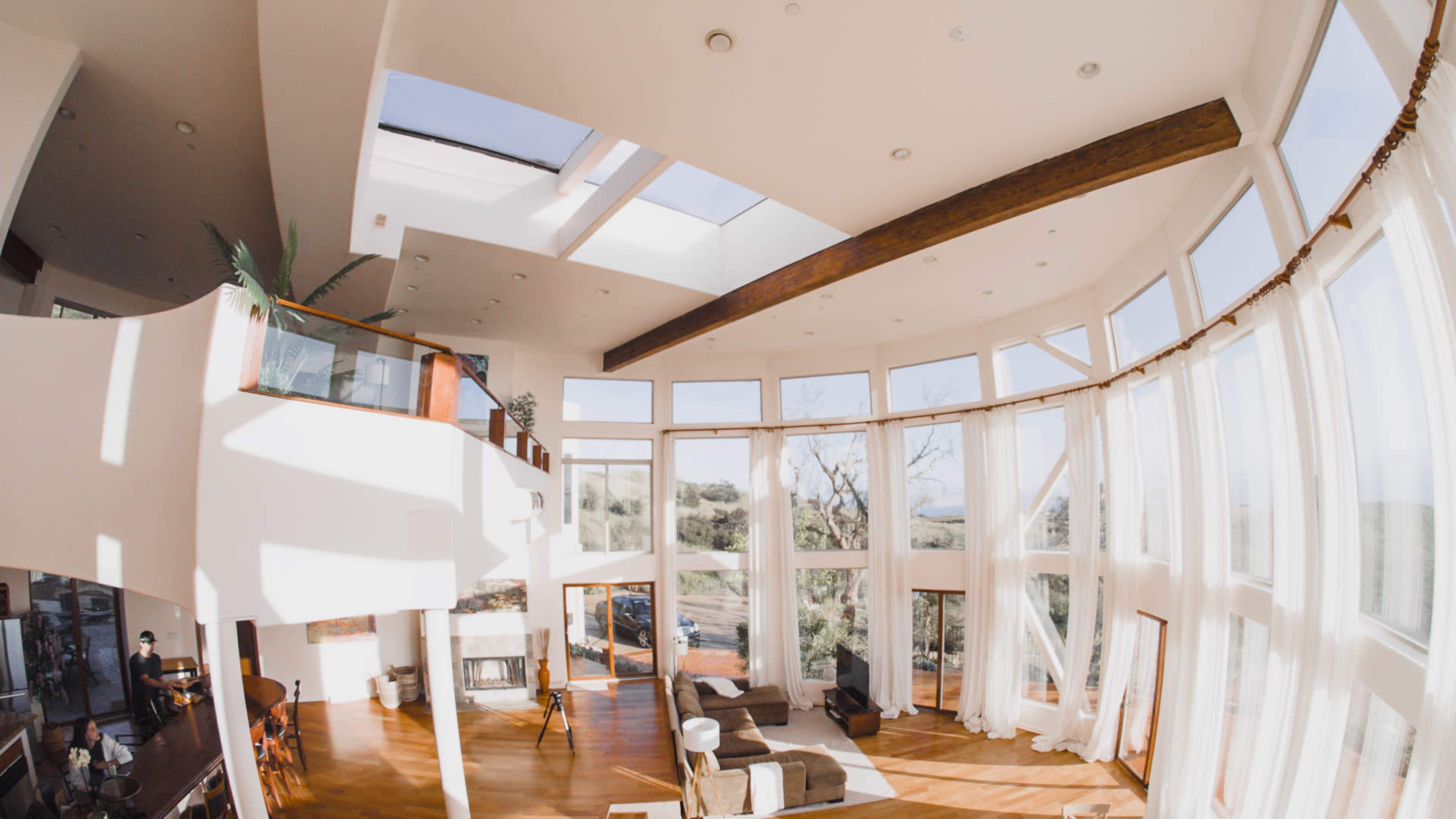 A spacious, sunlit living room with large windows, wooden beams, and modern furnishings.