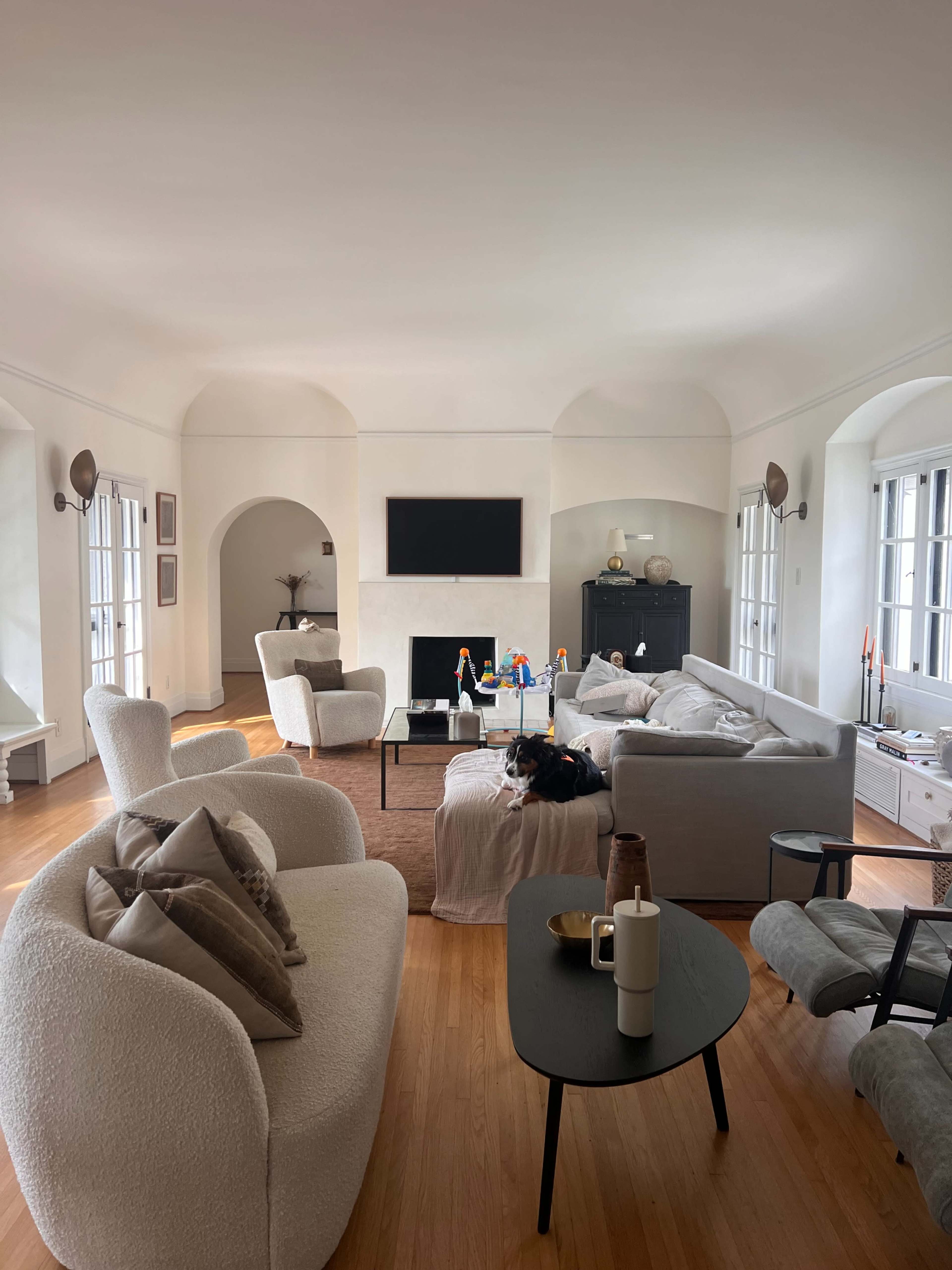 A spacious living room features light-colored furniture, a dark wooden coffee table, and a wall-mounted television above a fireplace.