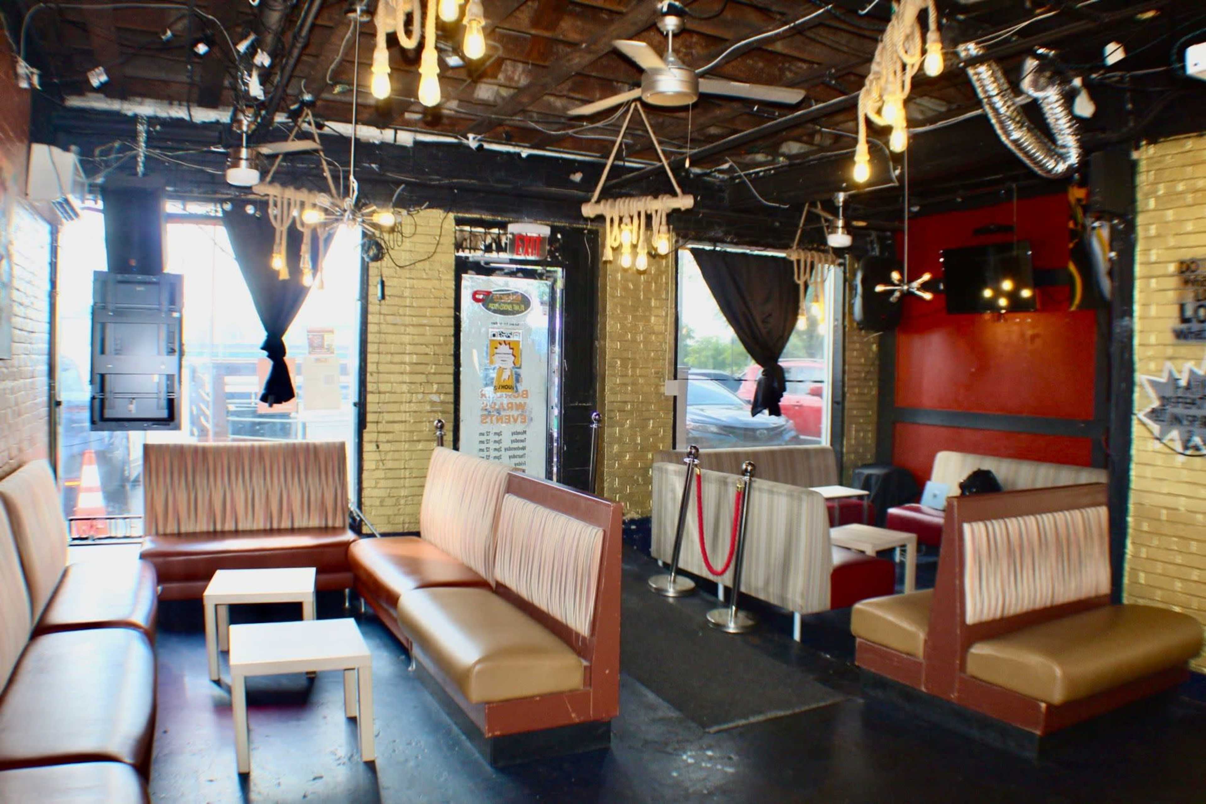 The image shows a dimly lit lounge with stylish seating, exposed brick walls, and hanging light fixtures, creating a casual atmosphere.