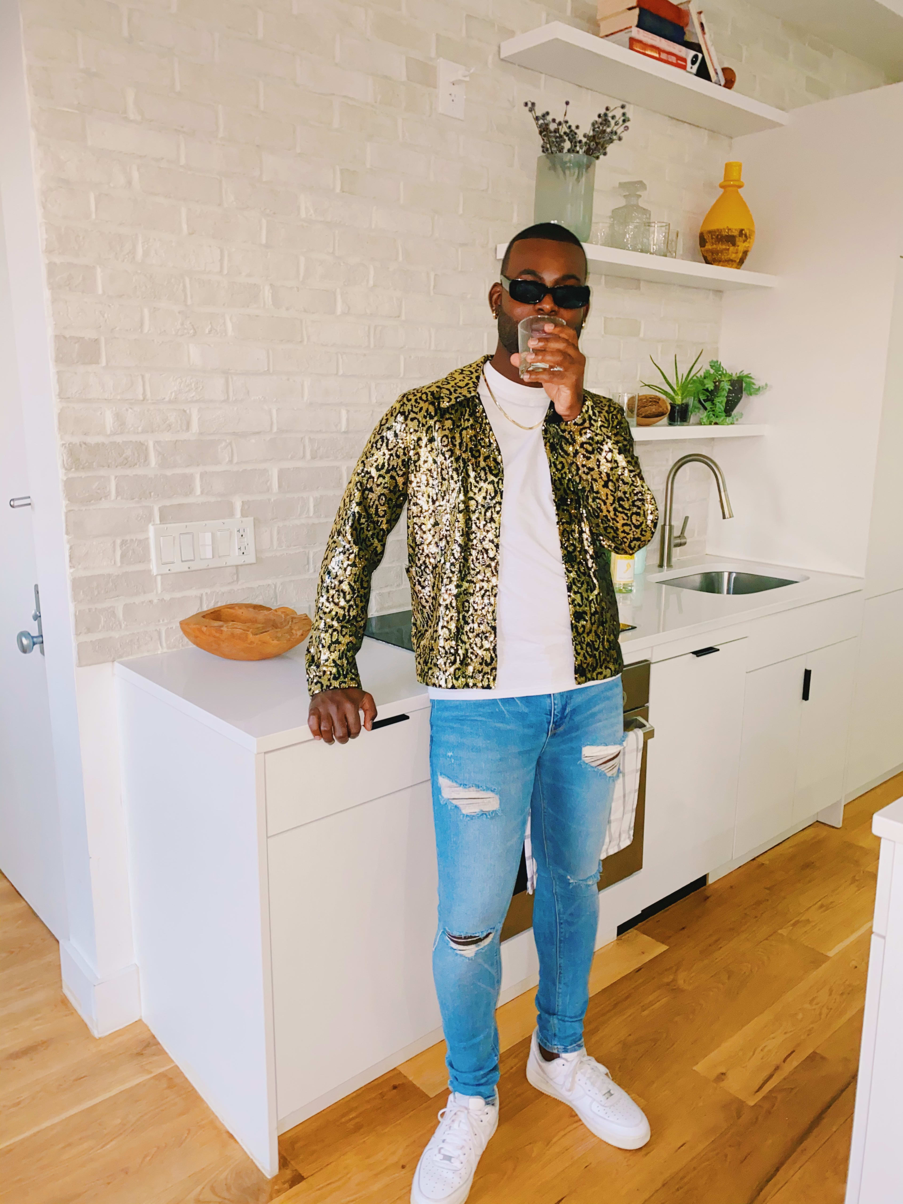 Un hombre posando en una sesión de fotos de moda junto a un fregadero en la cocina.