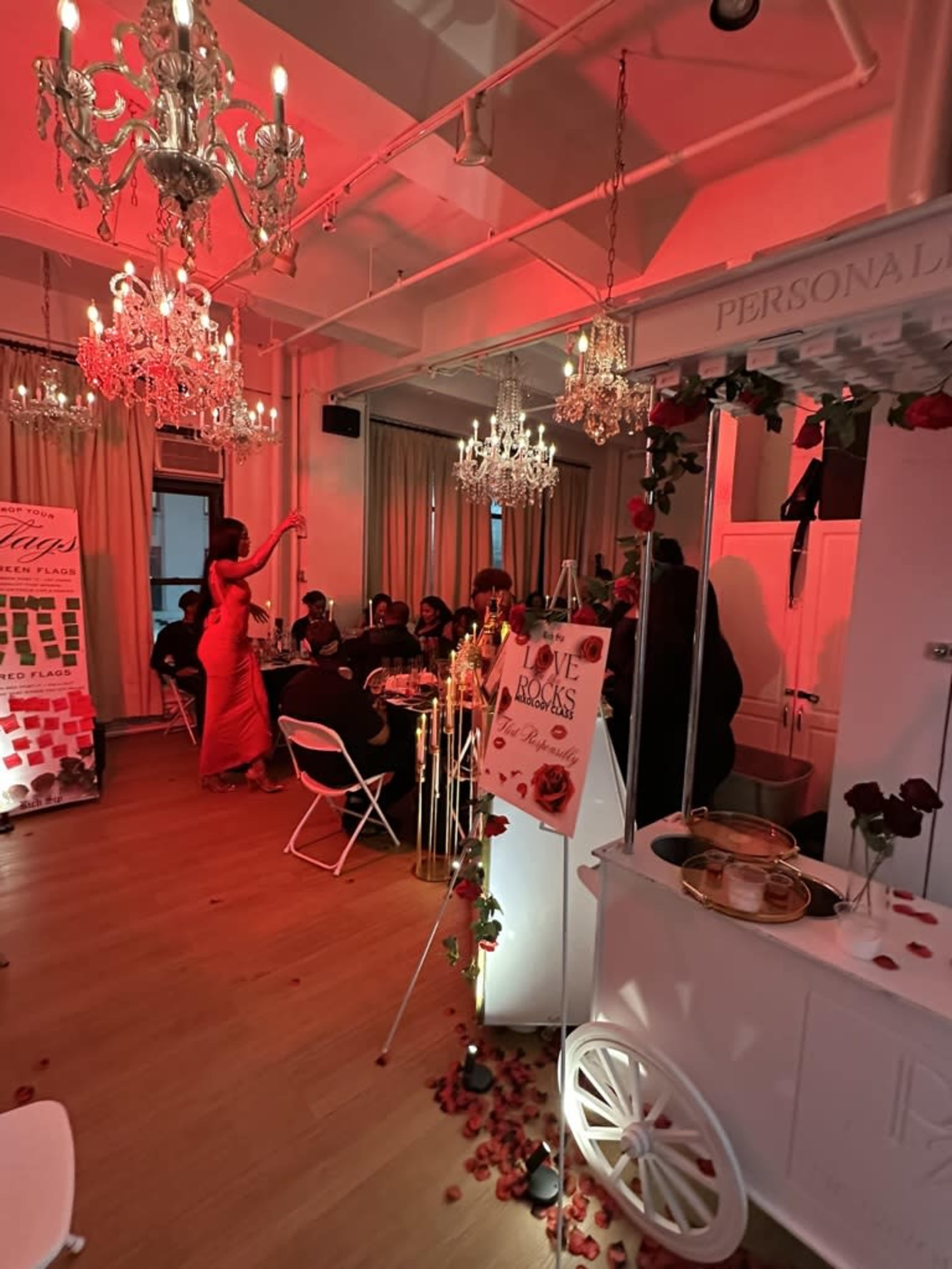 A formal dining event takes place in a room illuminated by red lighting, featuring several crystal chandeliers and decorated tables.