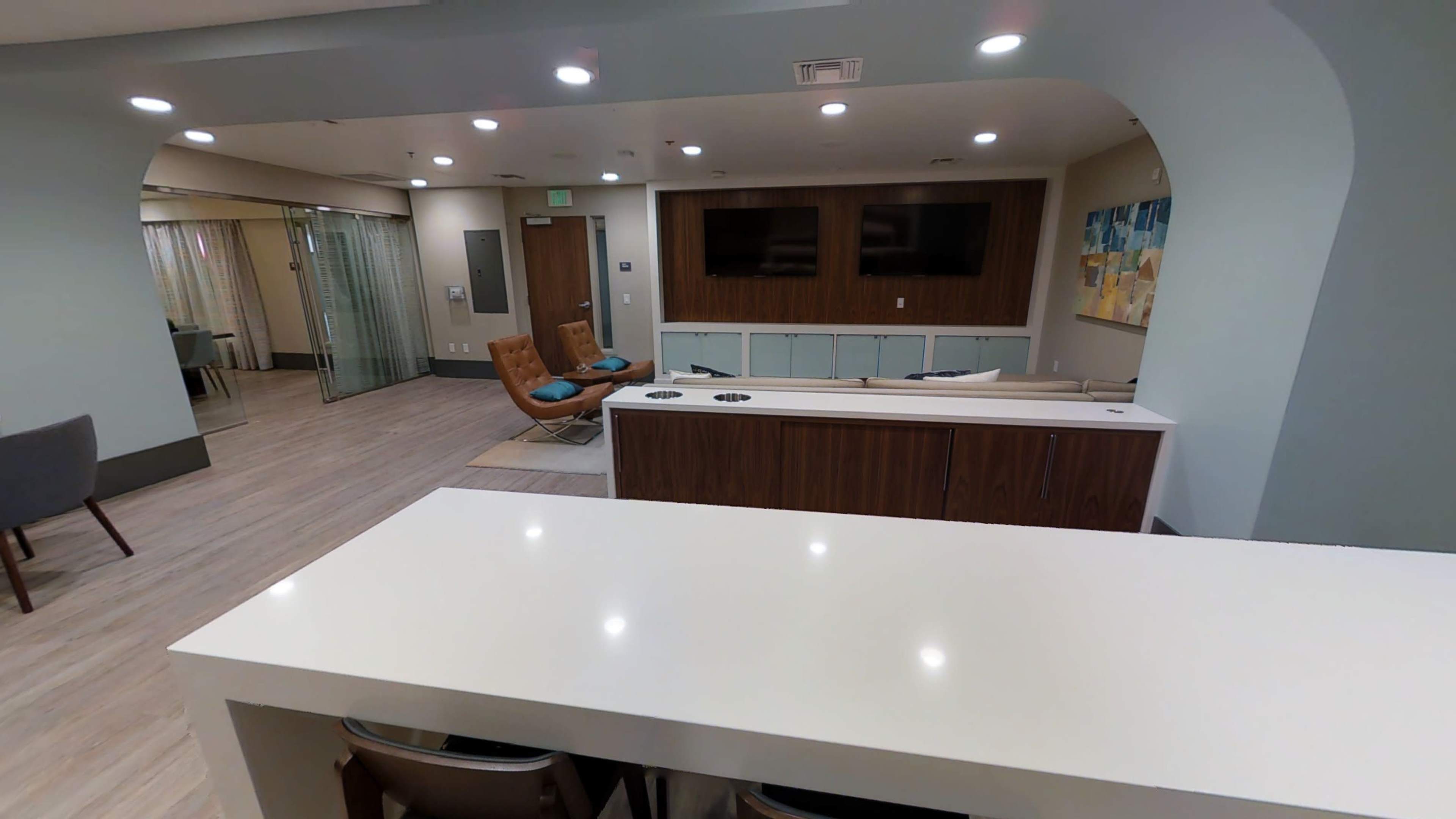 A modern communal lounge area featuring seating, a large television, and a counter with bar stools.