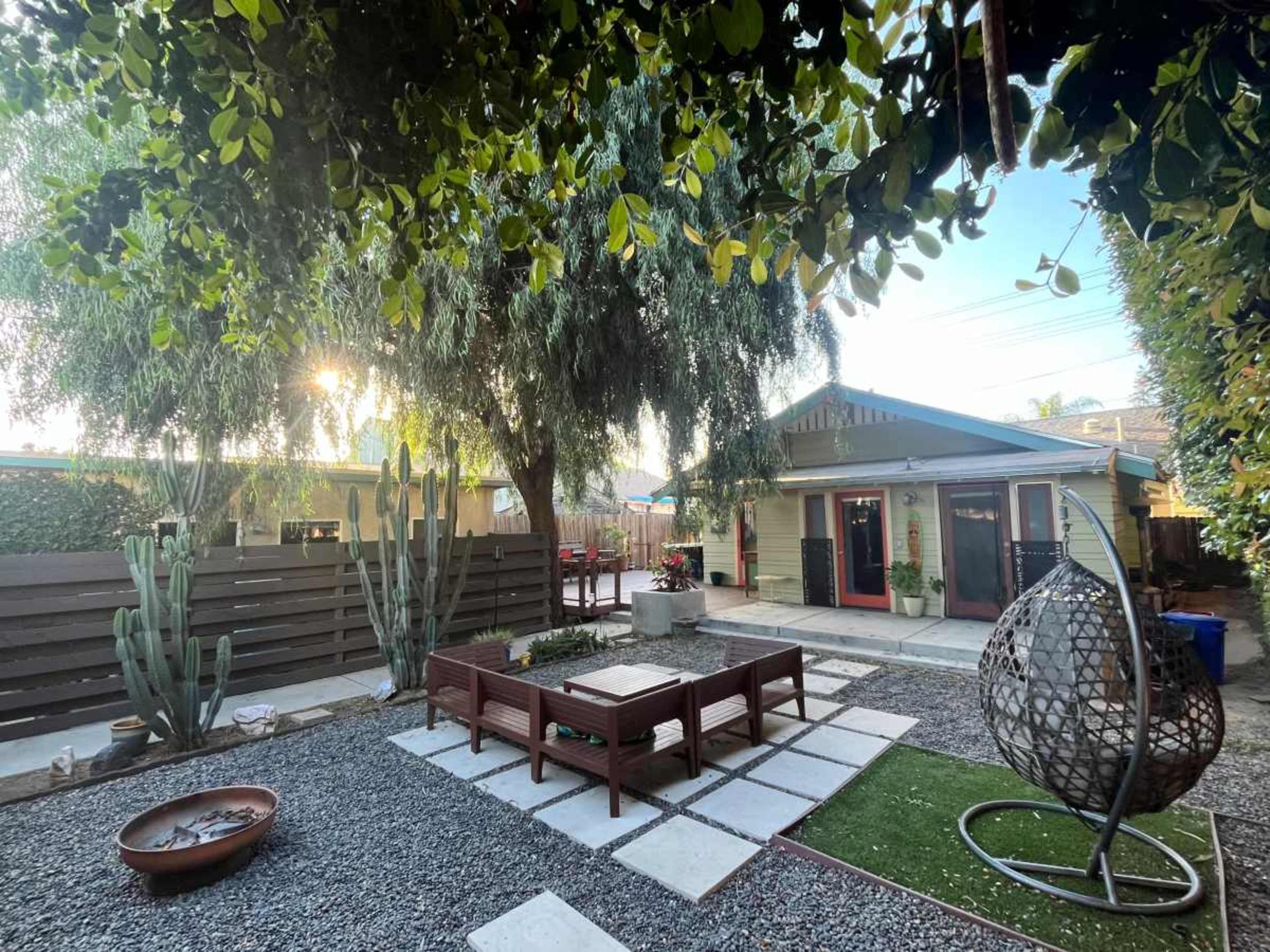 The image shows a landscaped backyard with patio furniture, gravel paths, and surrounding greenery.