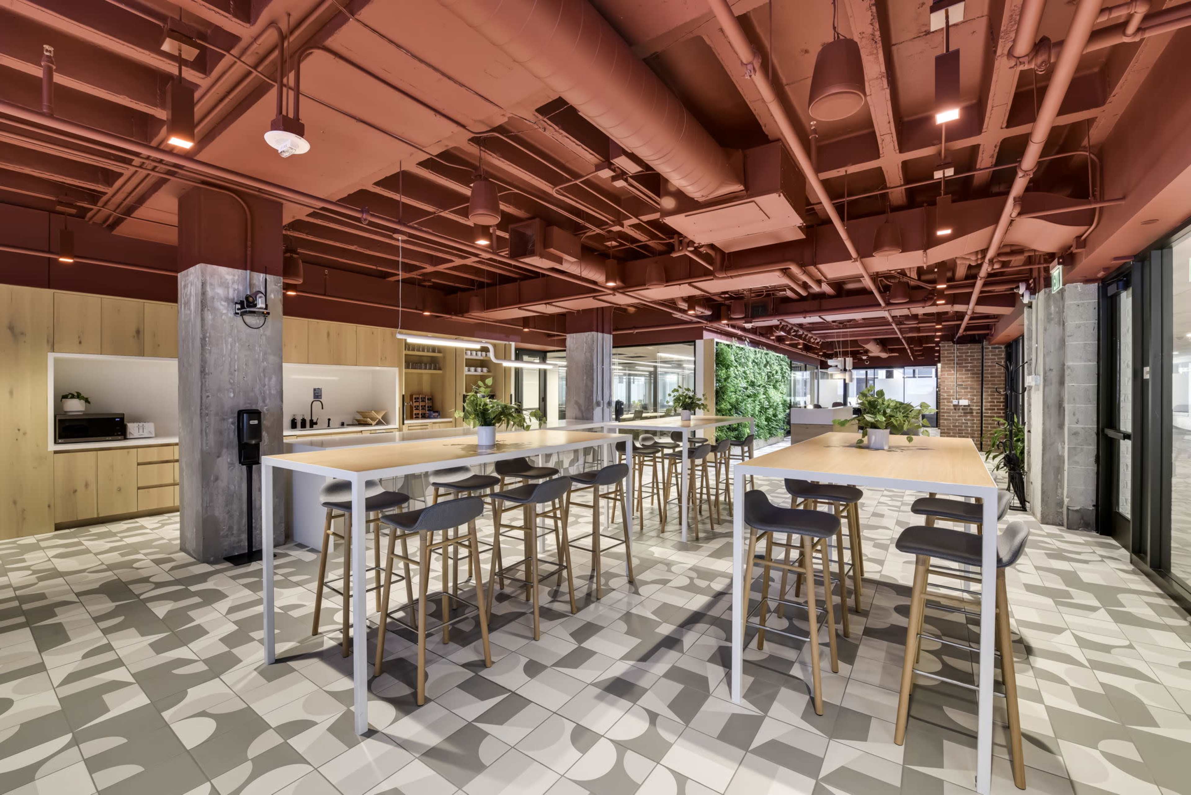 A modern interior café with high tables and seating, exposed piping, and greenery in a contemporary space.