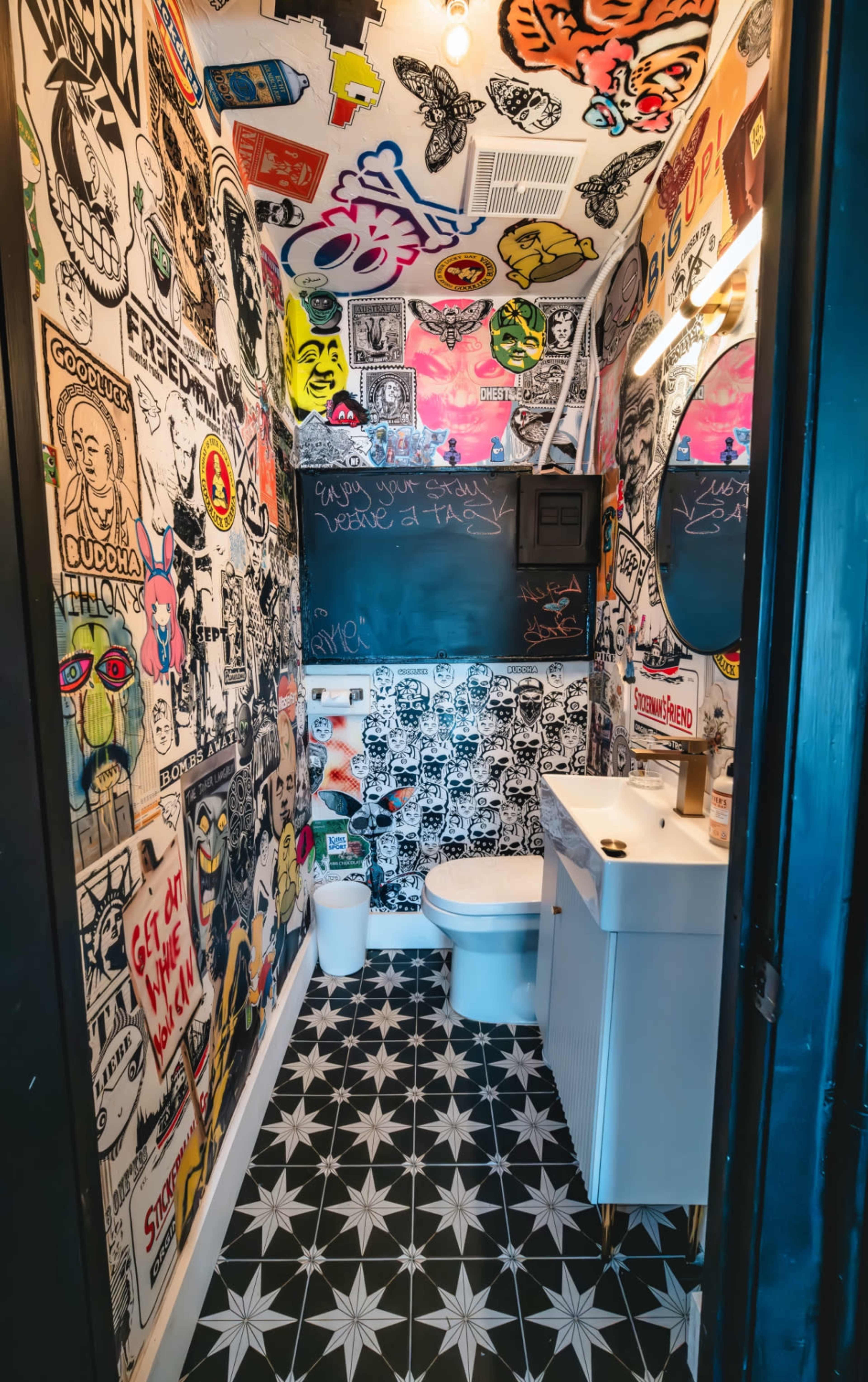 A small bathroom features a wall covered in colorful graffiti-style art and a patterned floor.