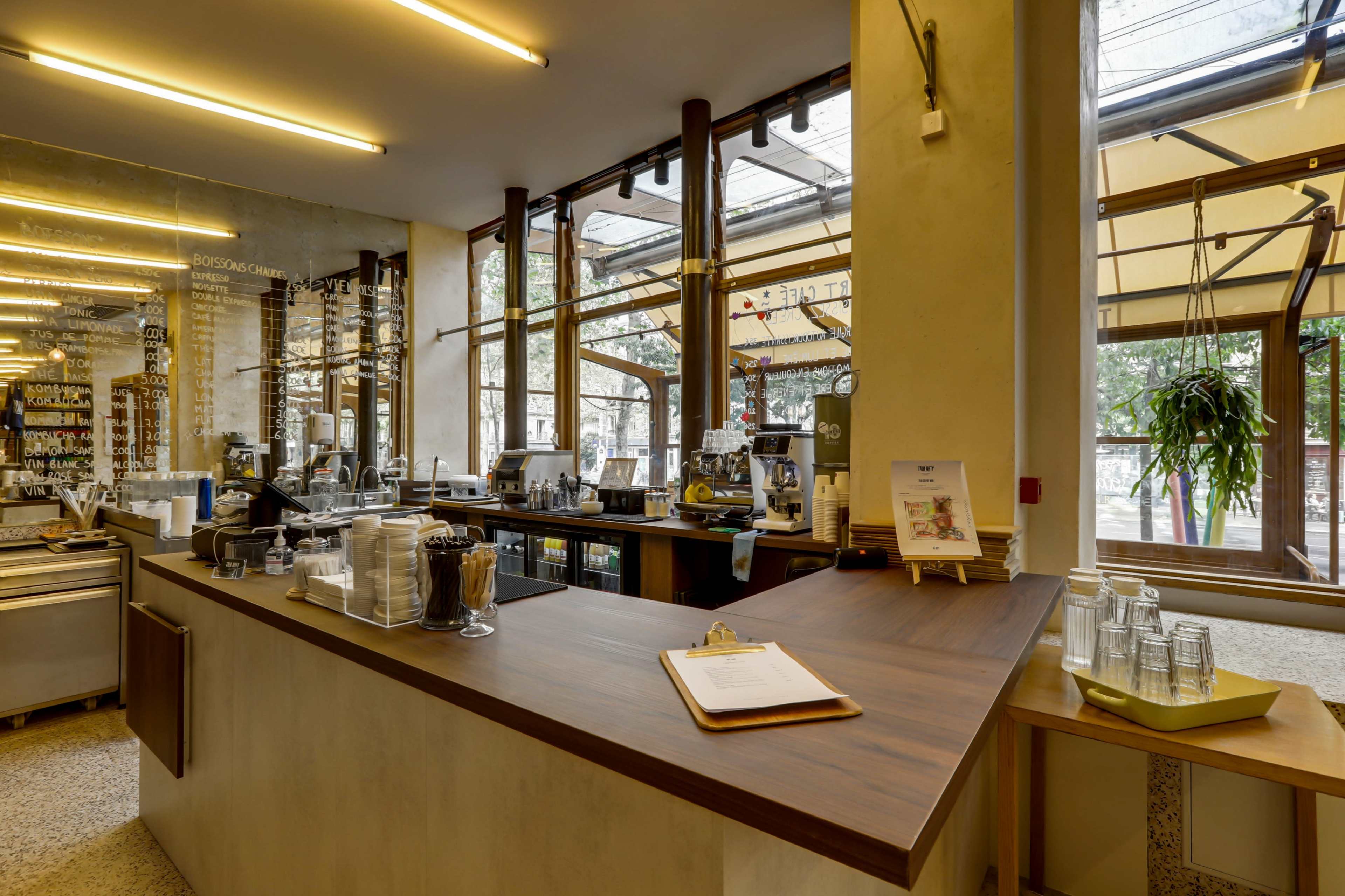 The image depicts a modern café interior with a wooden counter, glass display cases, and large windows allowing natural light to enter.